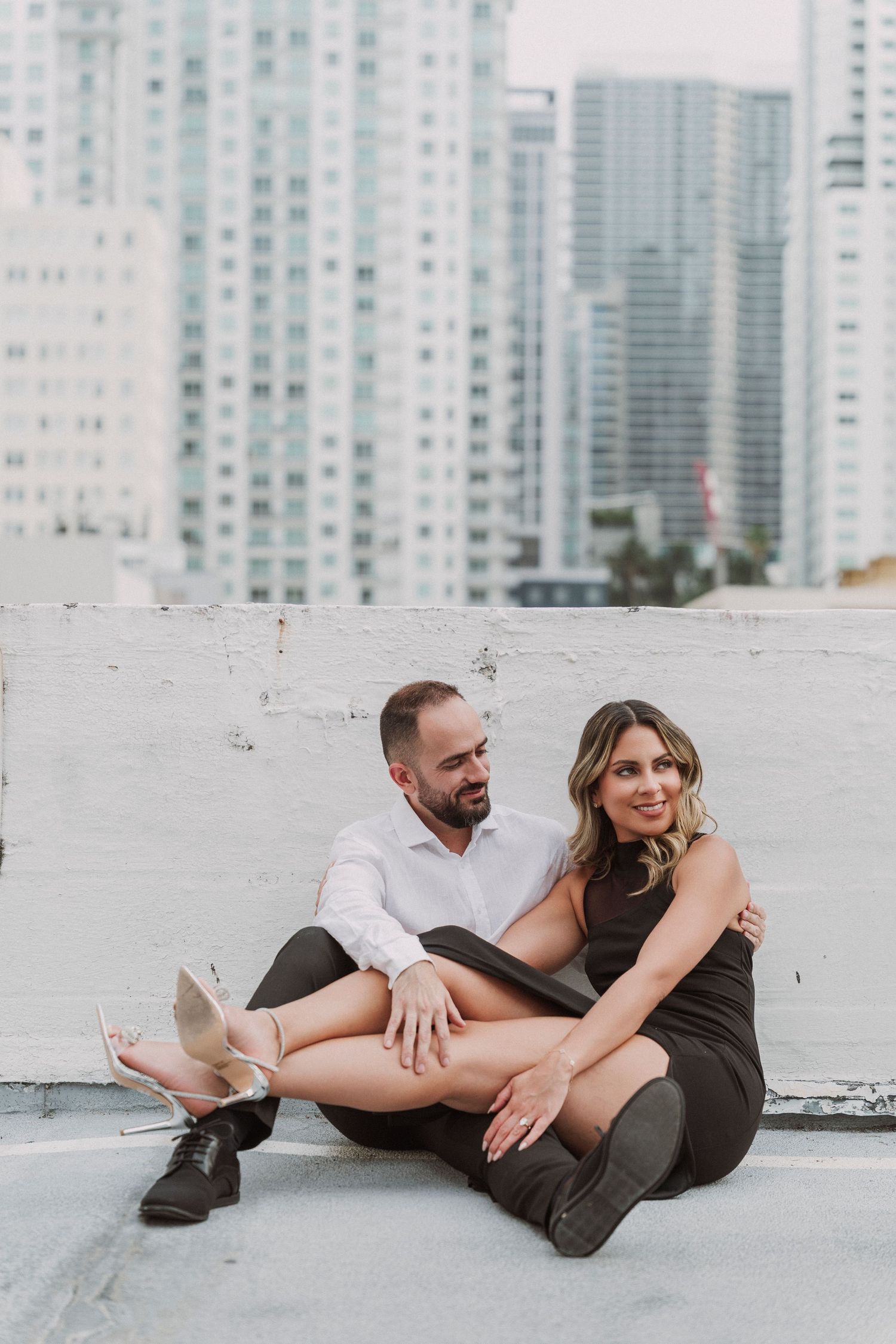Urban rooftop portrait of a couple sitting casually with city skyline in background.