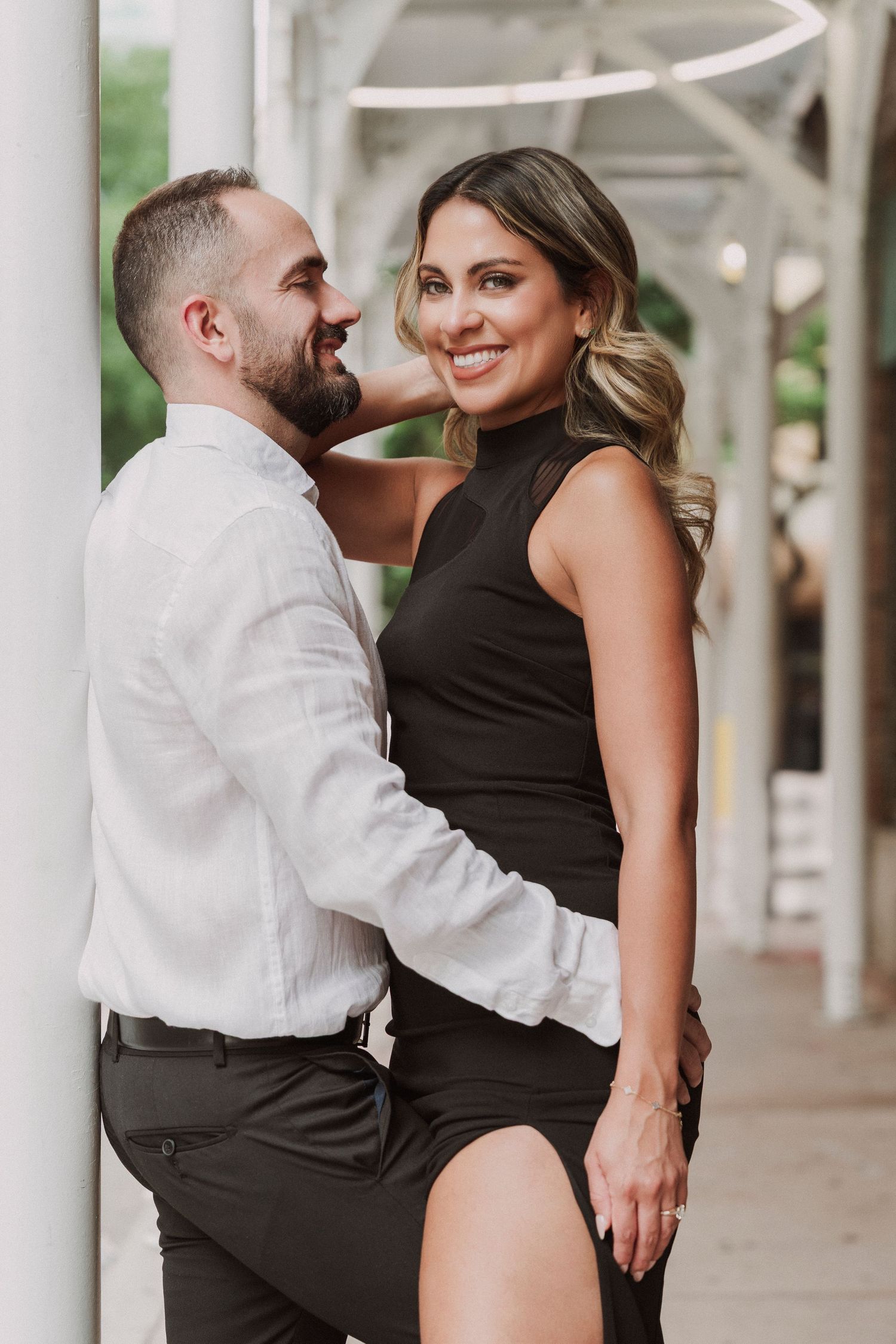 Couple sharing a romantic moment in formal attire under covered walkway.