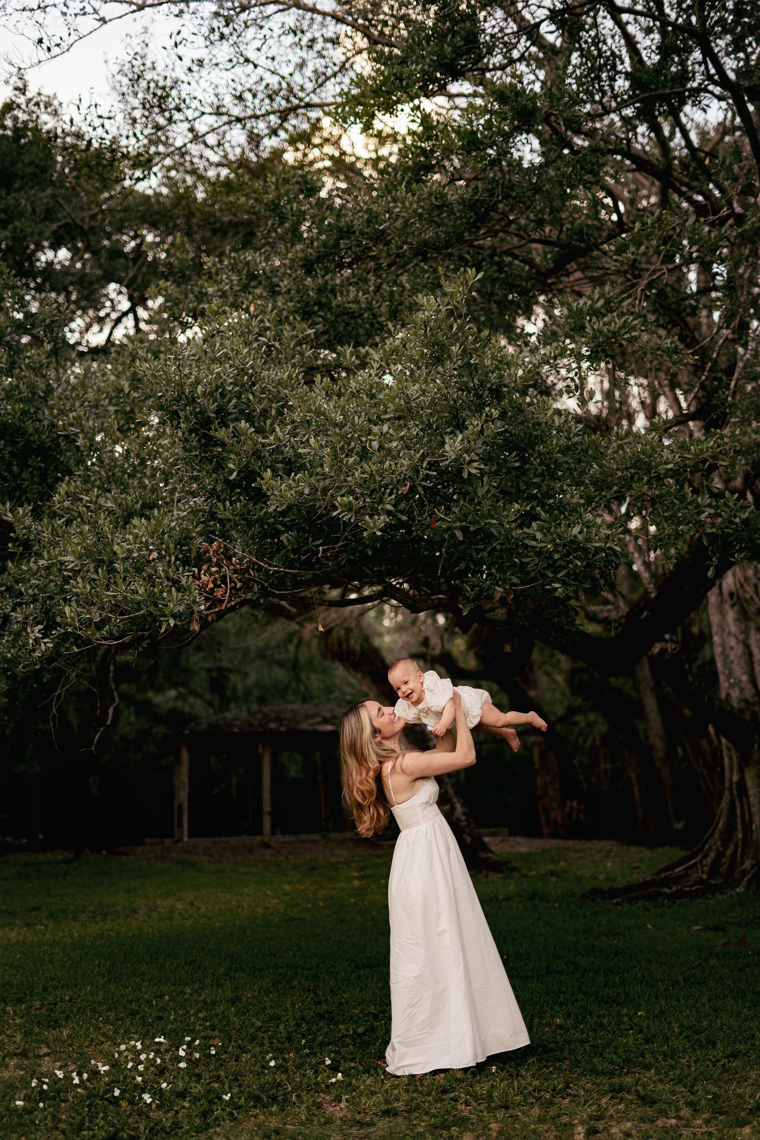 Mother and child in white dresses dance together in garden at sunset.