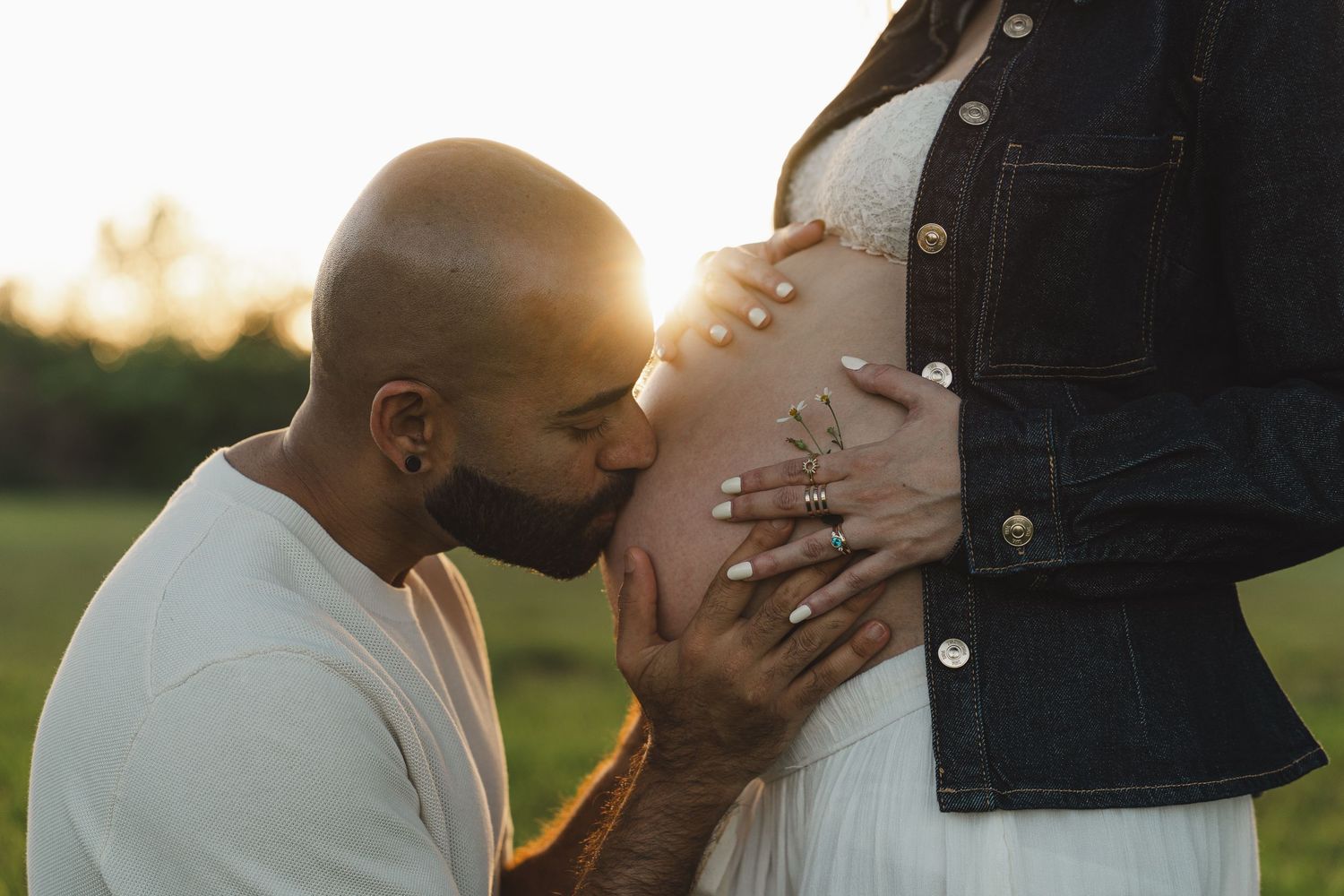 A tender moment captured during a maternity photoshoot outdoors at sunset in a grassy field.