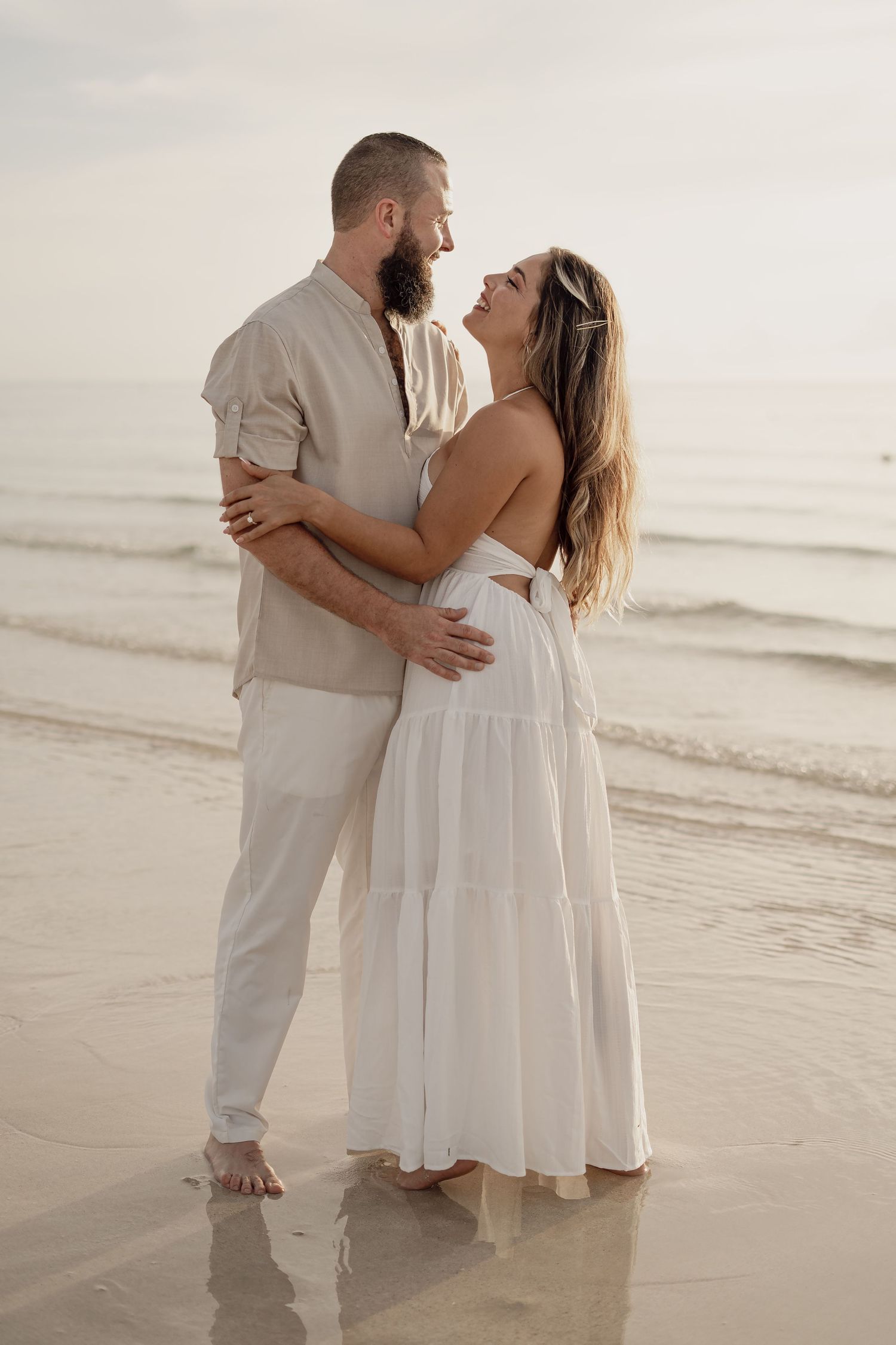Romantic sunset beach portrait of a couple in flowing white outfits.