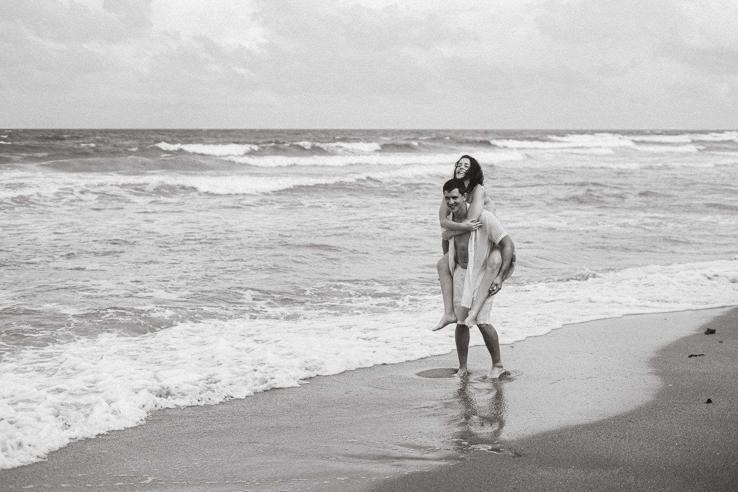 Black and white beach photoshoot showing playful moments near the ocean.