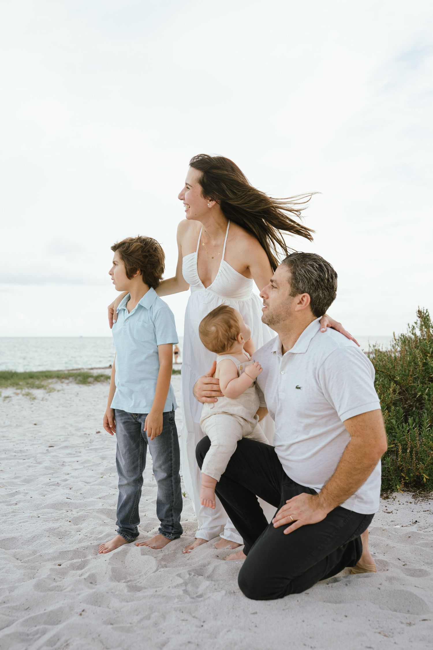 Family sitting together on beach sand while looking towards the ocean.