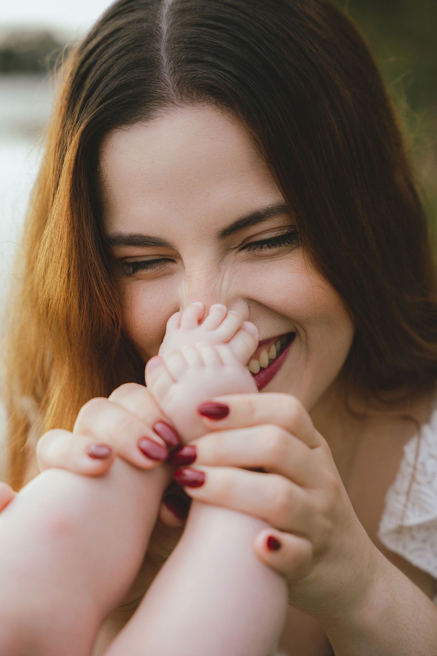 A joyful laugh captured in natural sunlight with burgundy nail polish.