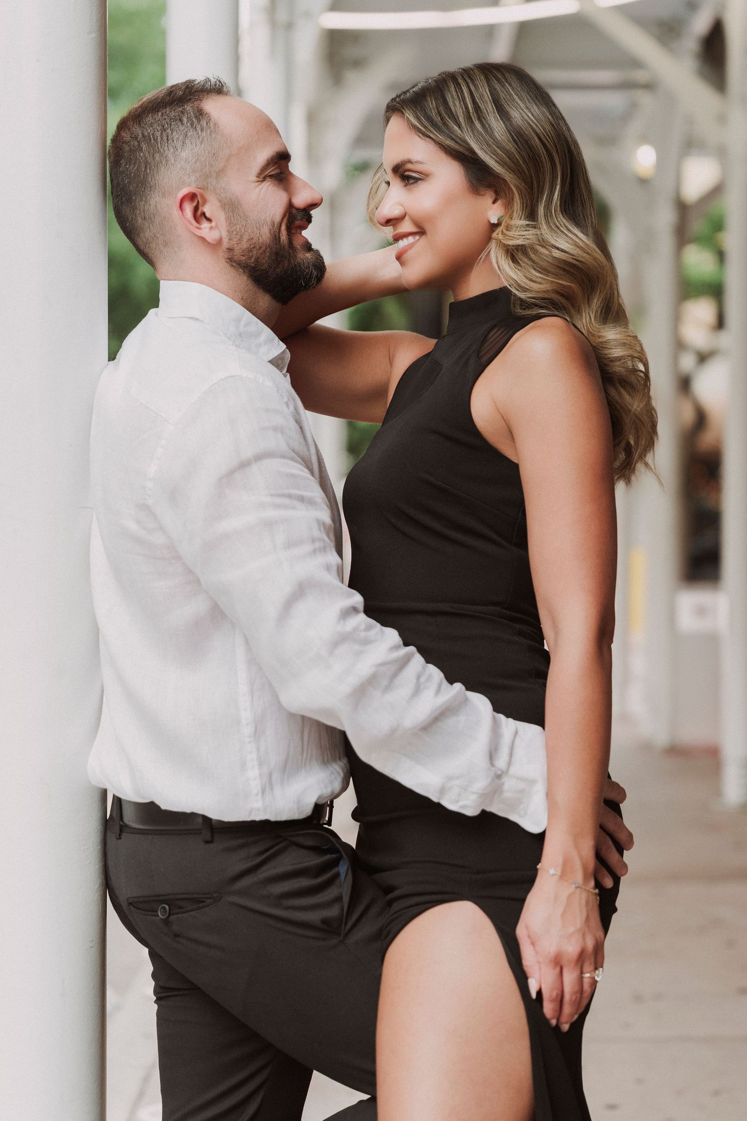 Stylish couple in formal attire pose intimately against a white column.