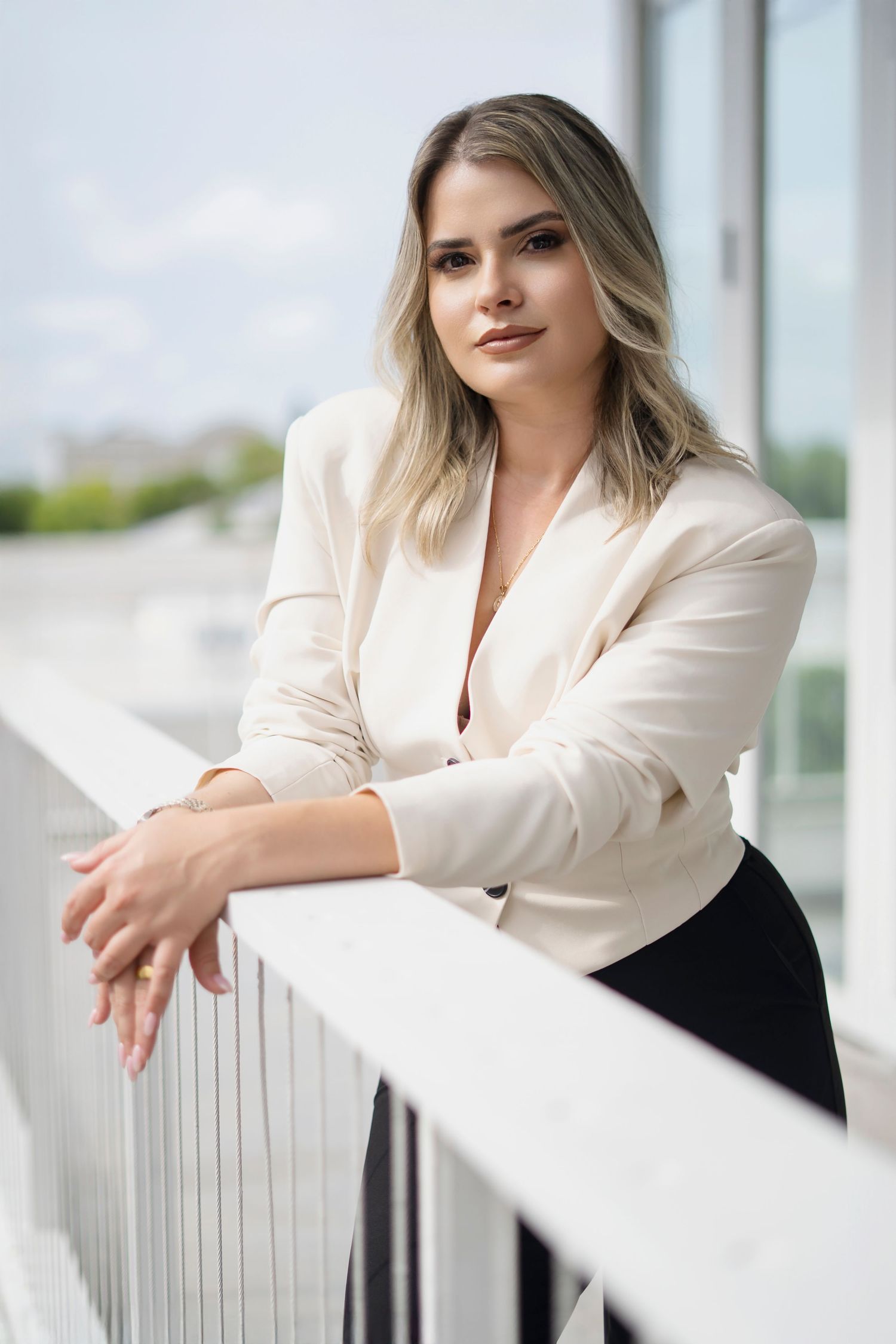 Professional portrait series of woman in white blazer leaning on railing.