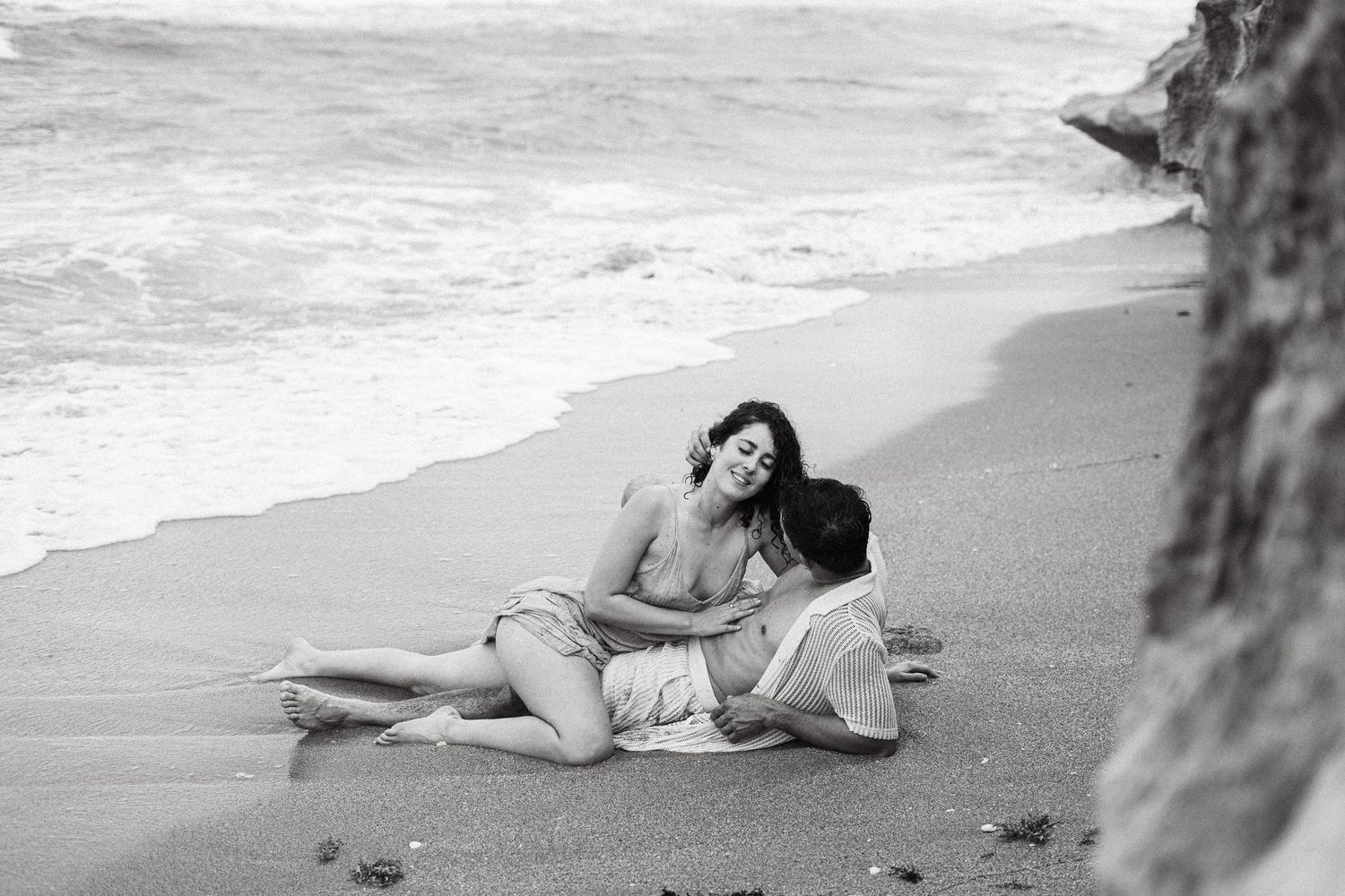 Romantic beach photoshoot with couple lying in gentle surf.