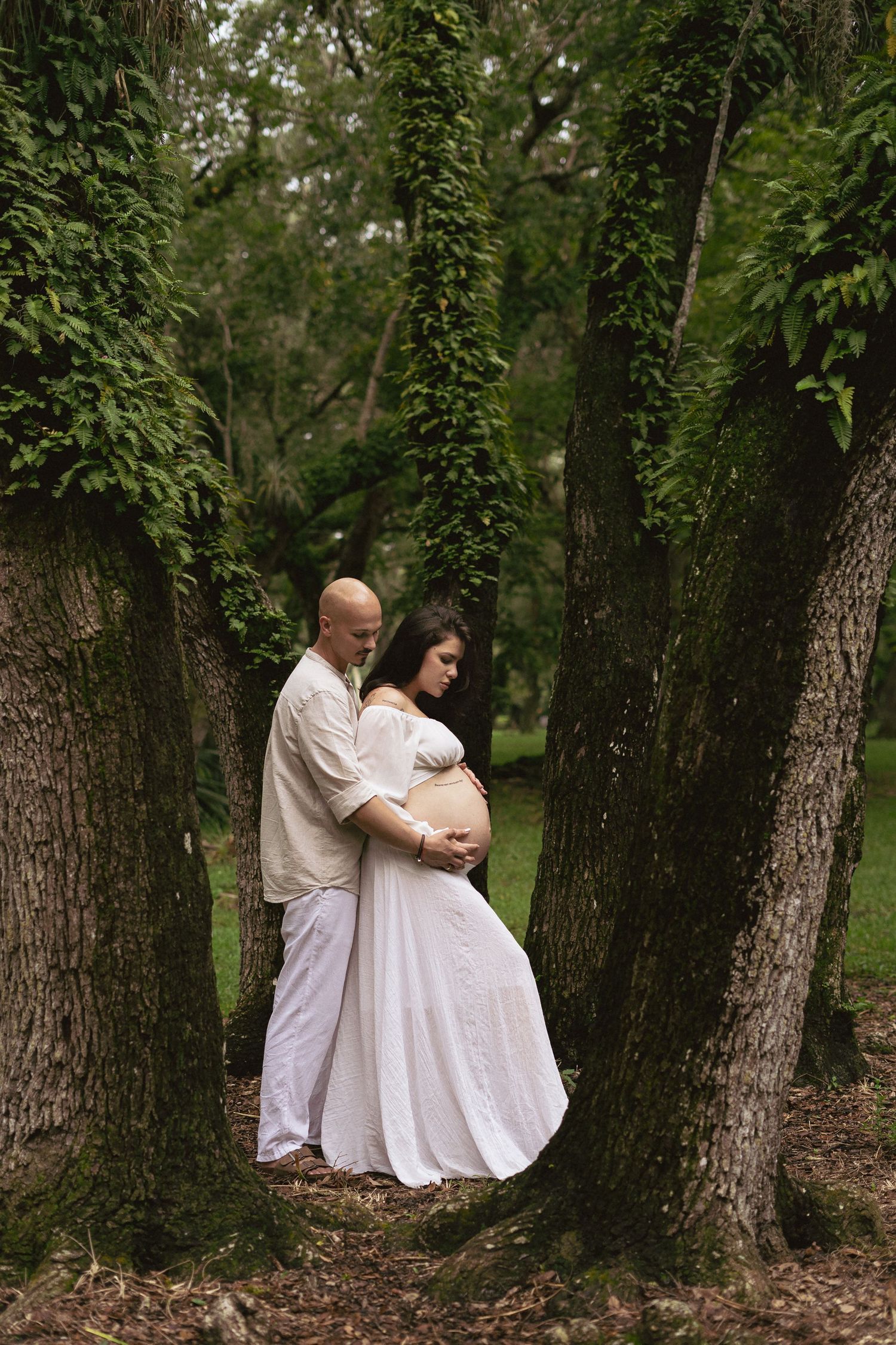 Family maternity photo in a wooded setting with everyone dressed in white.