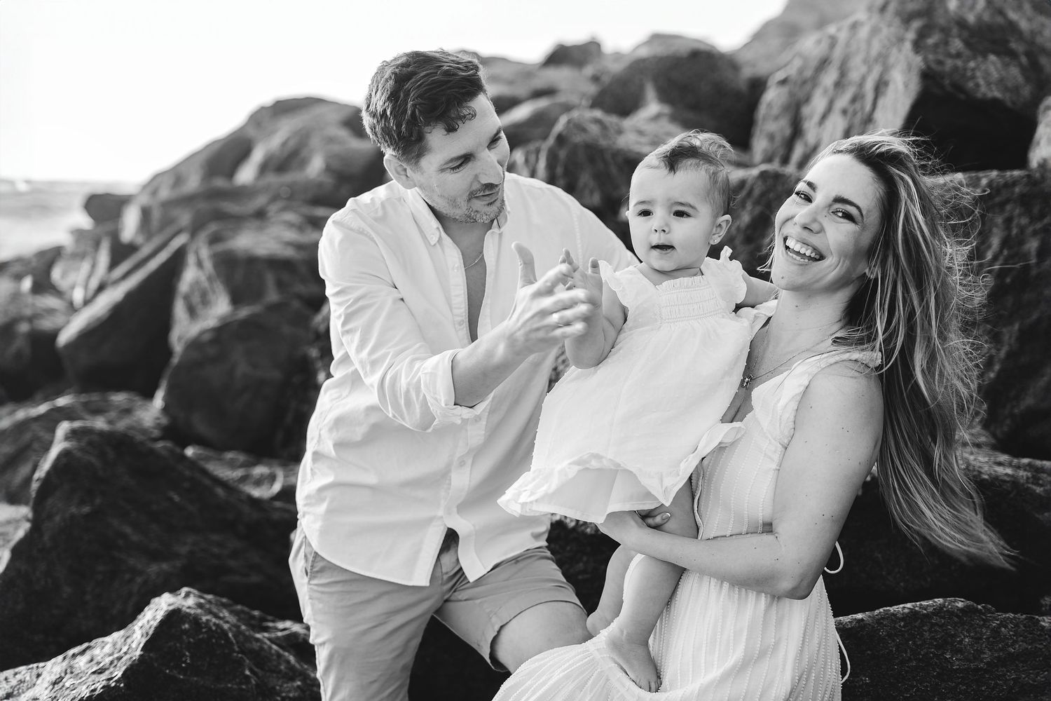 Family enjoying tender moments together on rocky beach landscape.