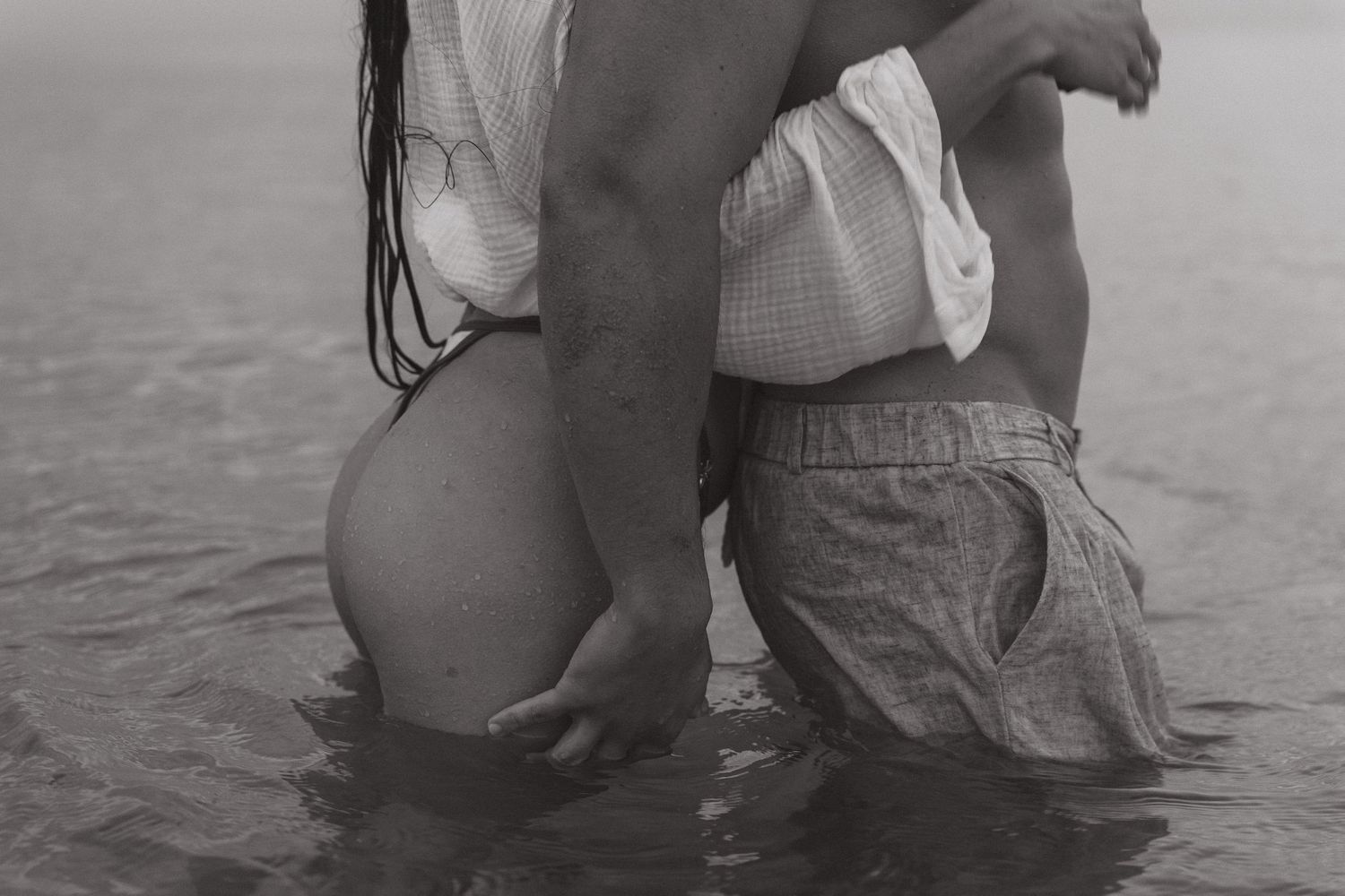 Black and white photo of couple embracing in shallow ocean water, romantic beach moment.