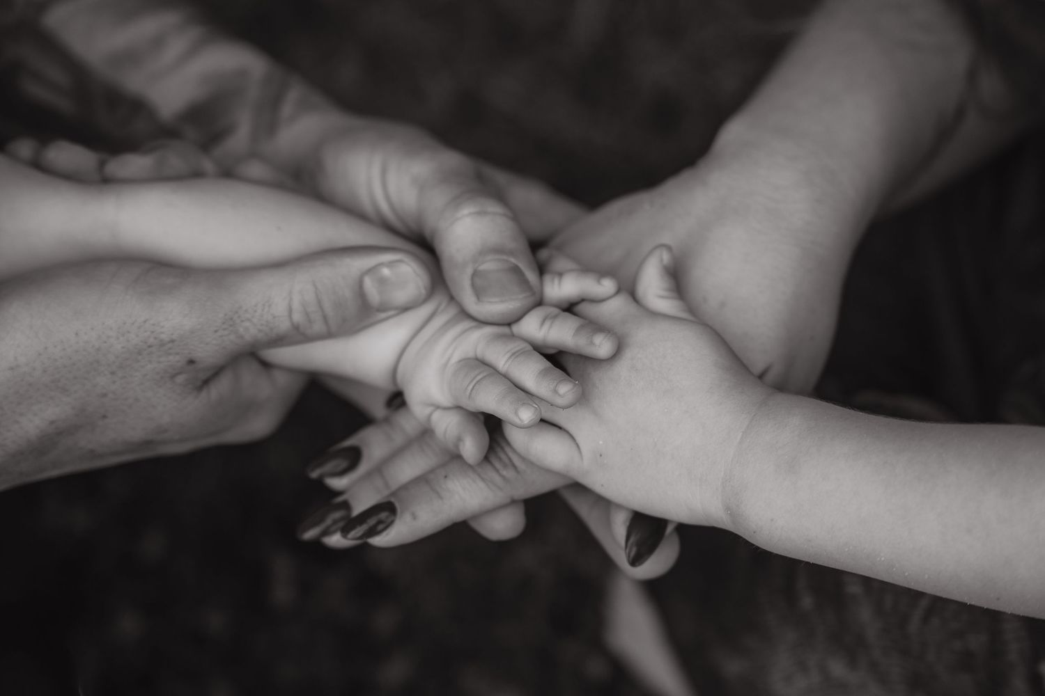 Black and white photo of multiple generations of family hands stacked together, symbolizing unity and love.