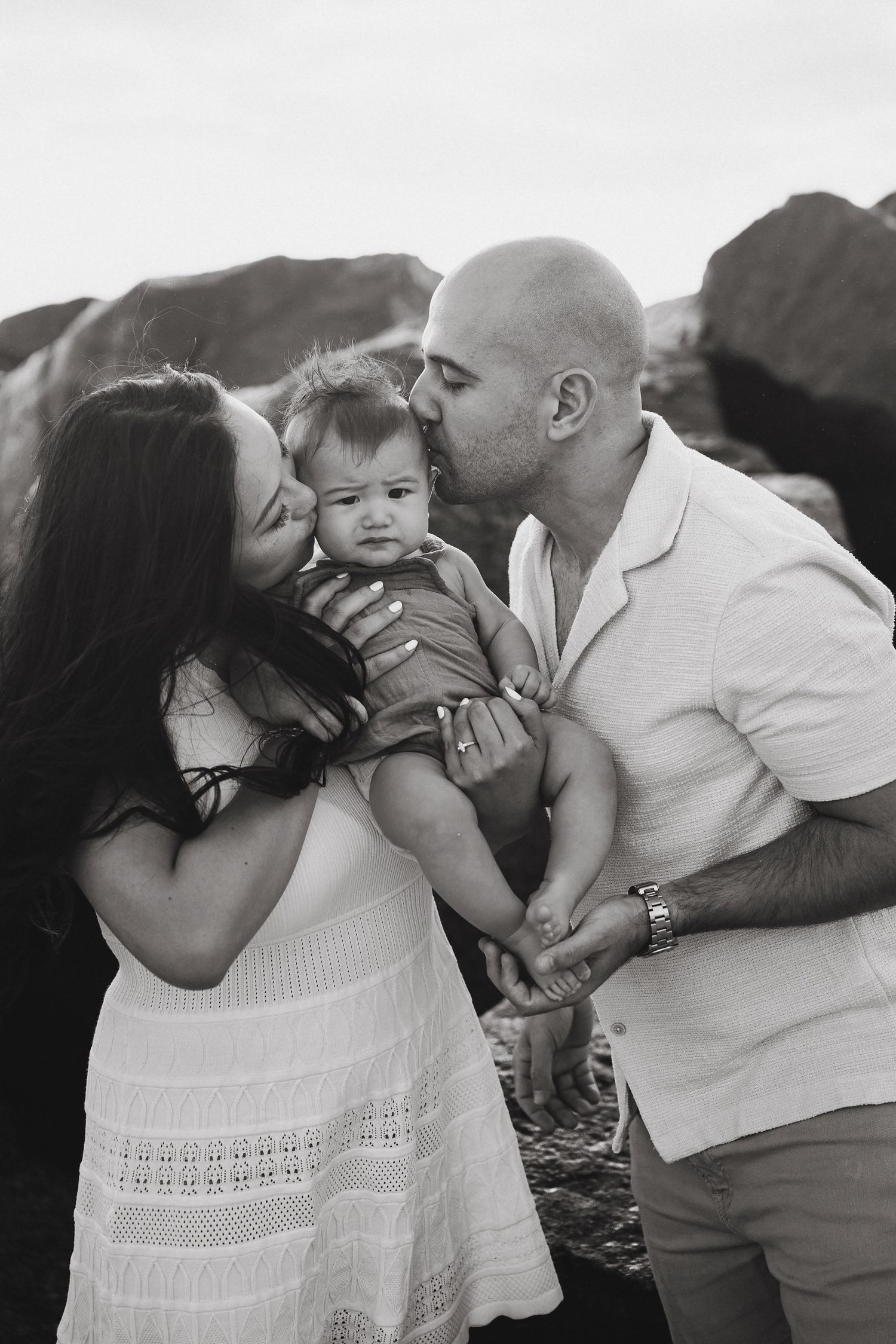 Family of three sharing kisses and cuddles on the beach.