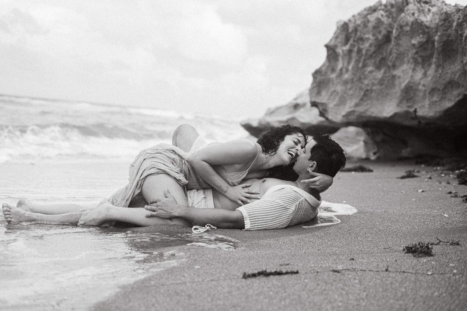 Black and white series of a couple lying together on a sandy beach.