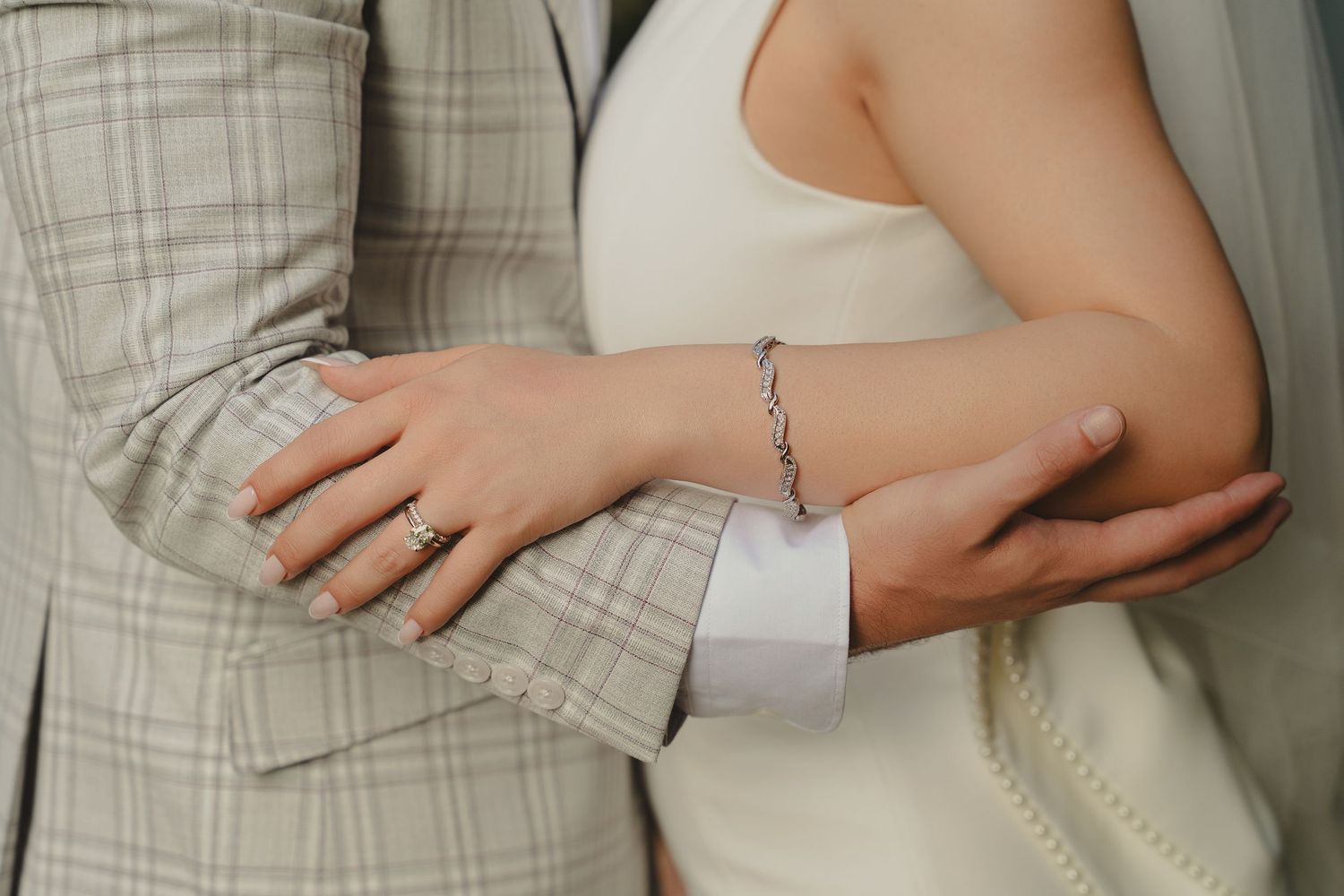 Close-up of a couple in wedding attire, woman wearing a diamond bracelet and ring, holding arms together.
