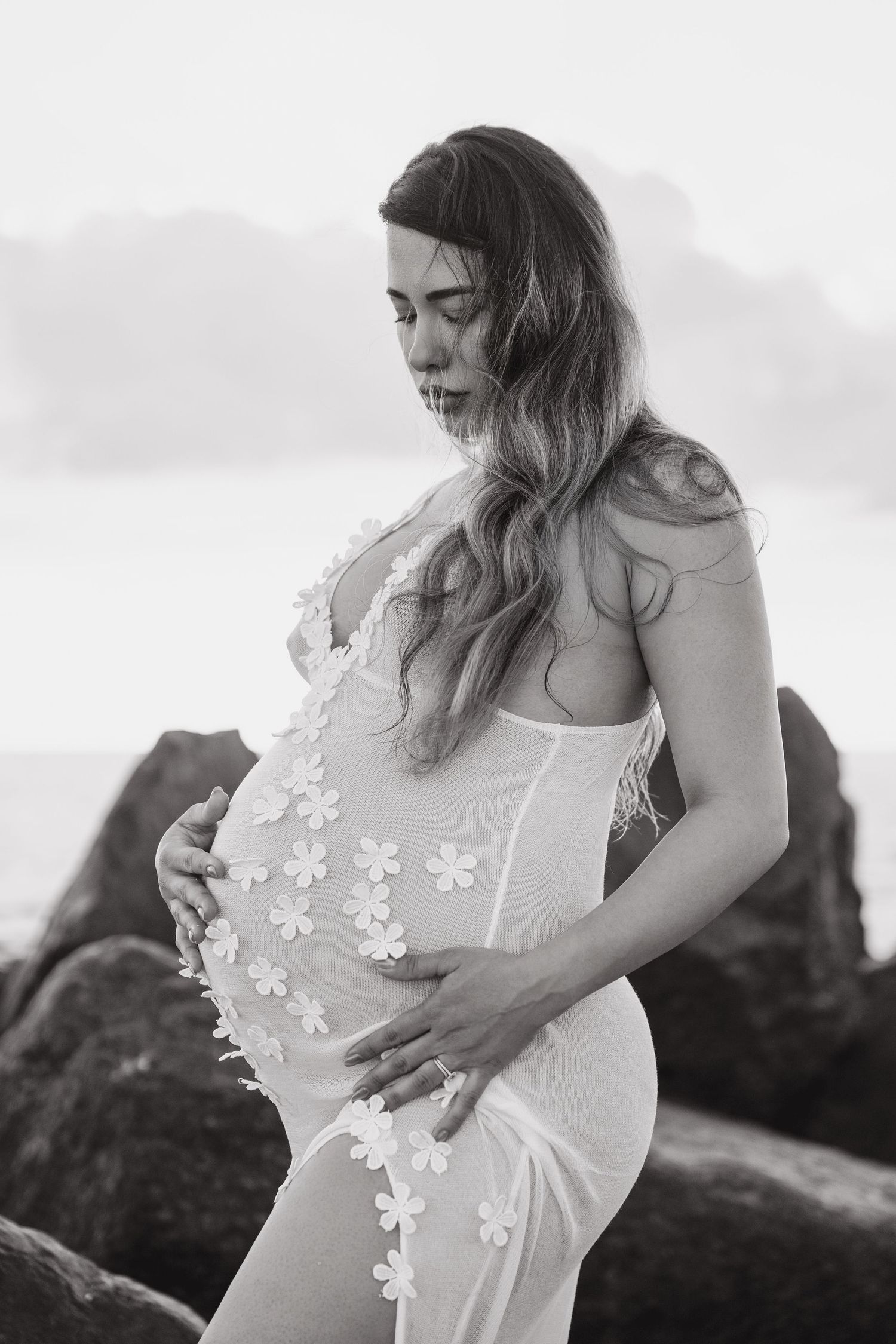Intimate maternity portrait with delicate white floral dress details against a moody sky.