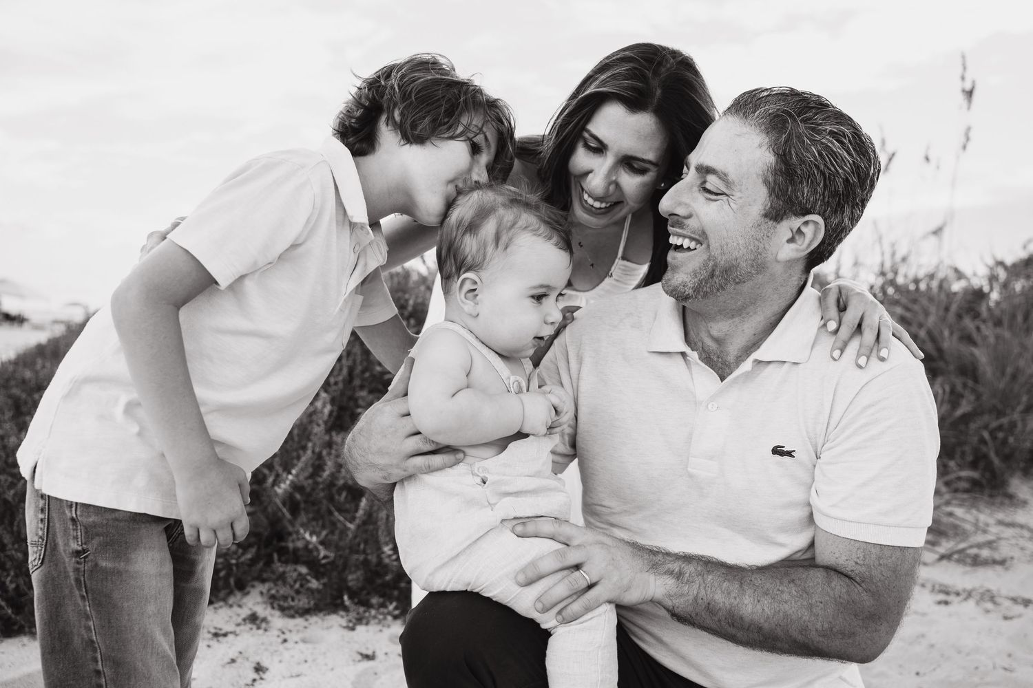 Candid family portraits captured on a white sandy beach with sea grass.