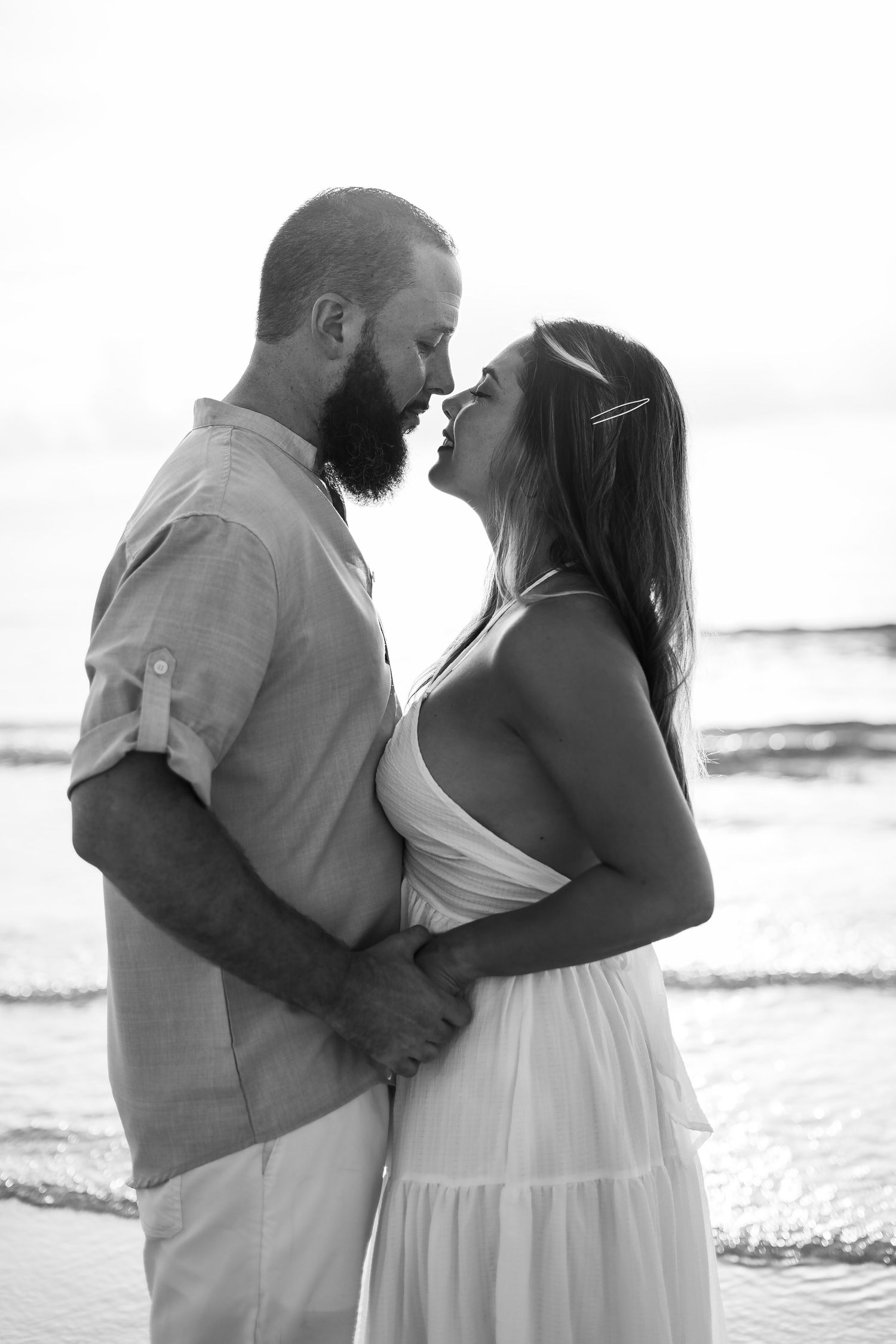 Black and white beach portrait of a couple in light summer clothing.
