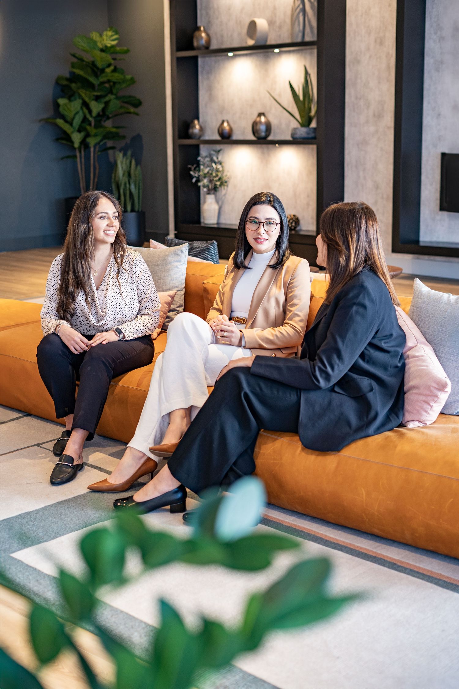 Casual business meeting on orange couch in modern office space with plants.