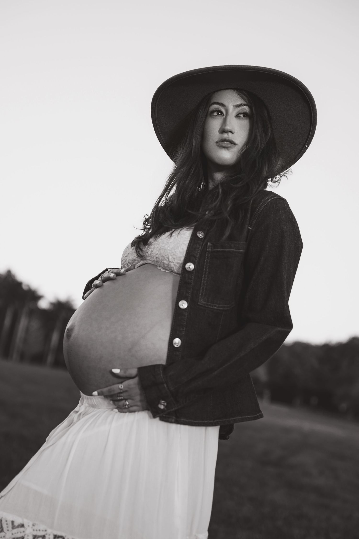 Black and white portrait series showing a figure in a wide brimmed hat and flowing dress standing in a field.