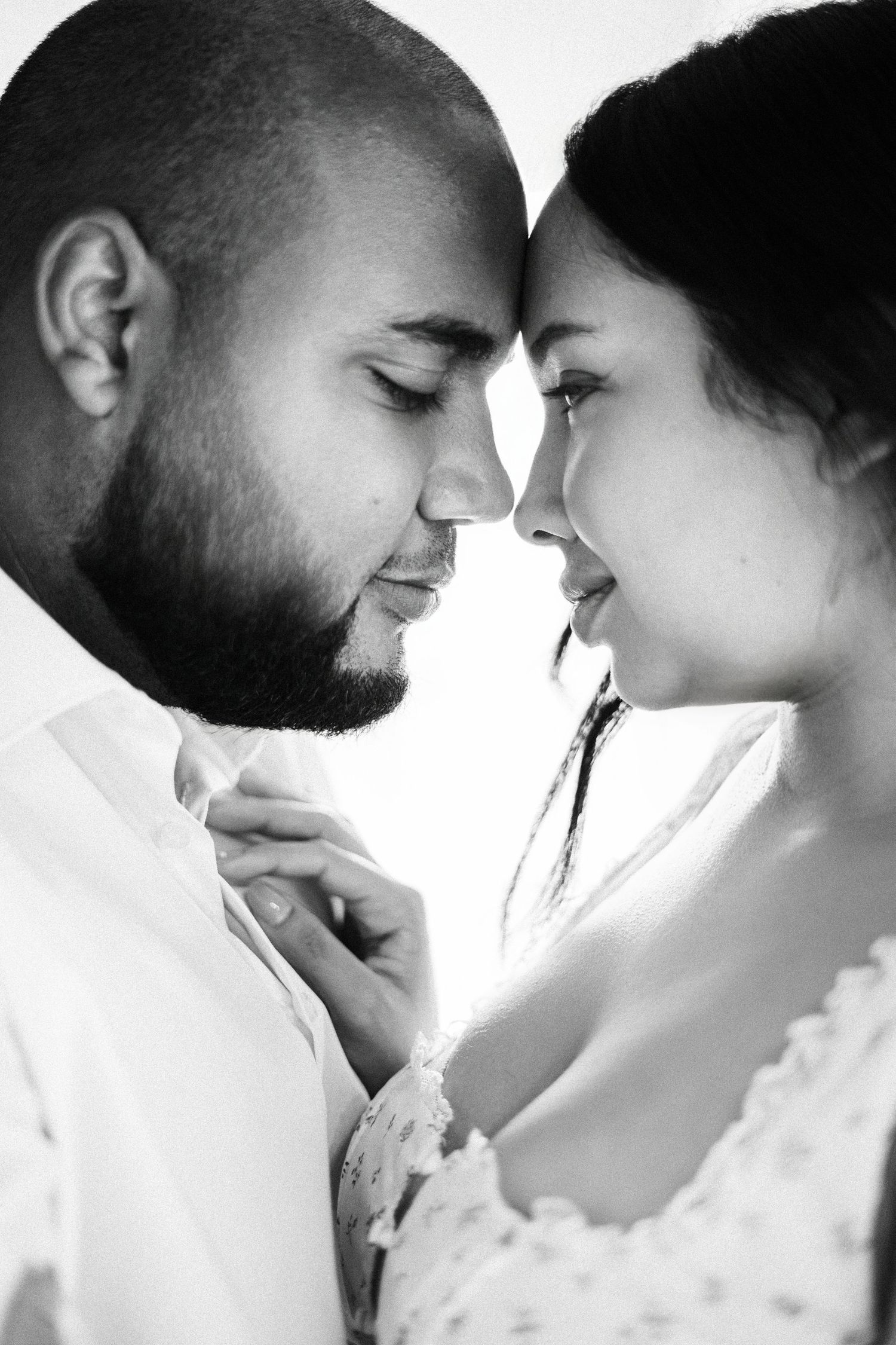 Black and white photo of a romantic couple with foreheads touching, sharing an intimate moment together.