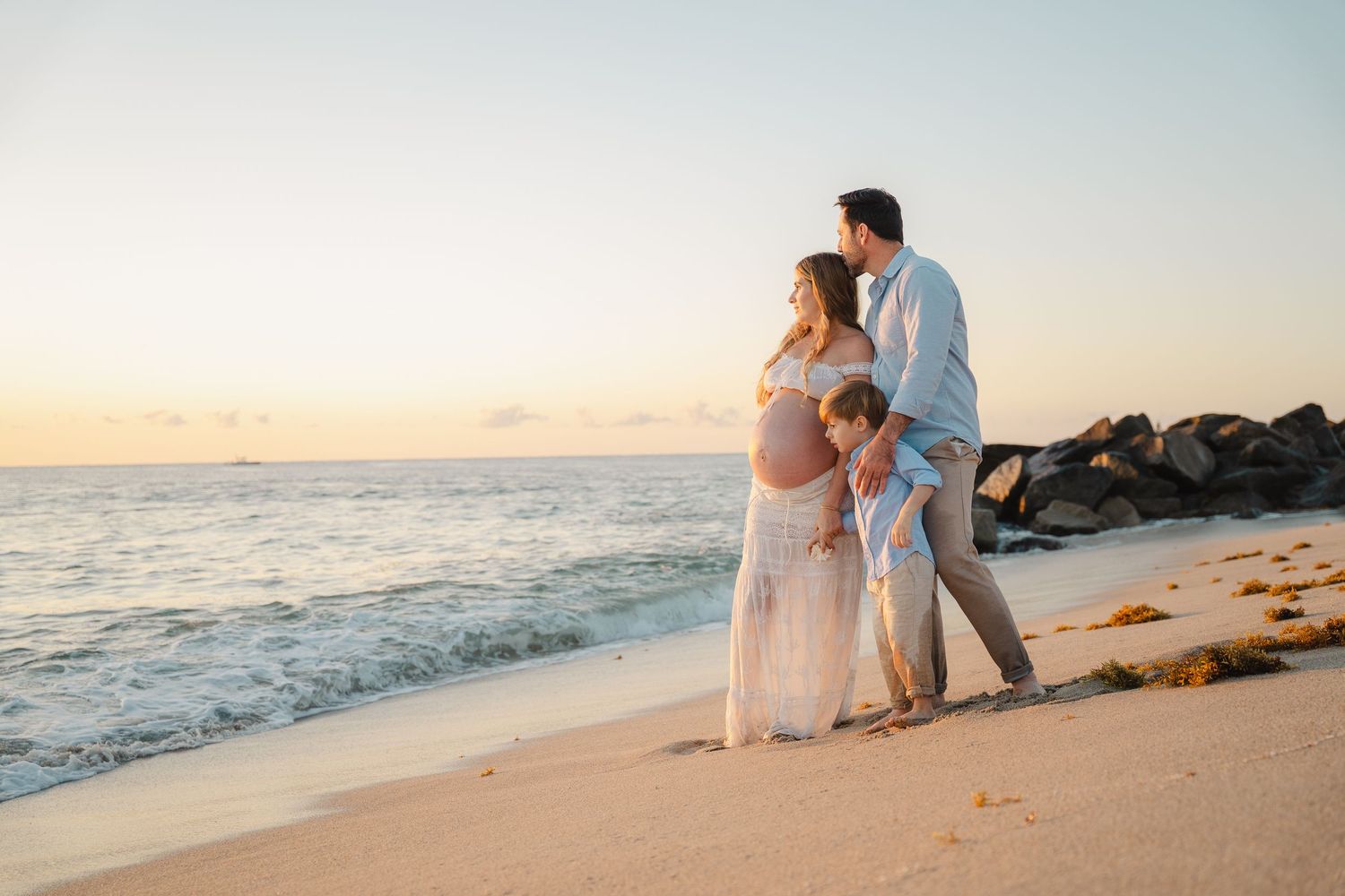 A couple walks along a serene beach at sunset with gentle waves rolling onto the sandy shore.