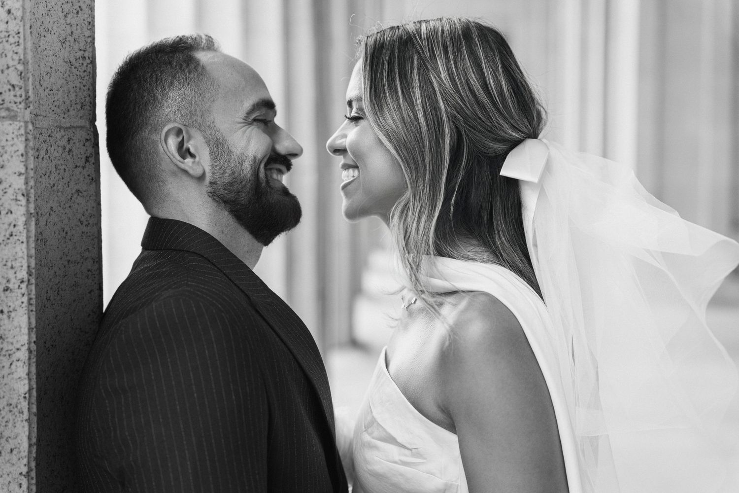 Intimate black and white portrait of a couple sharing a tender moment against a wall.