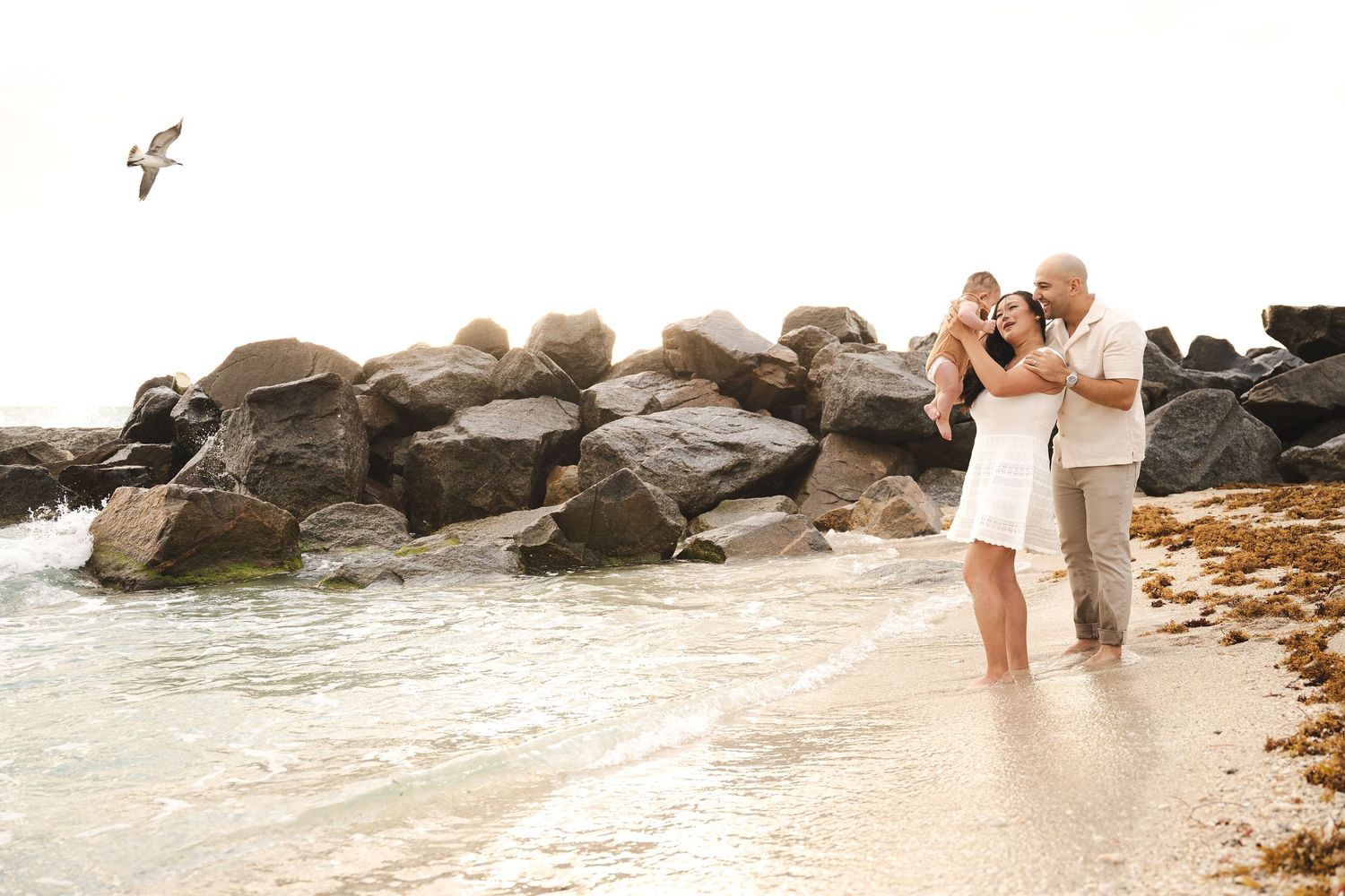 Family enjoying time together by the ocean with waves crashing on rocks.