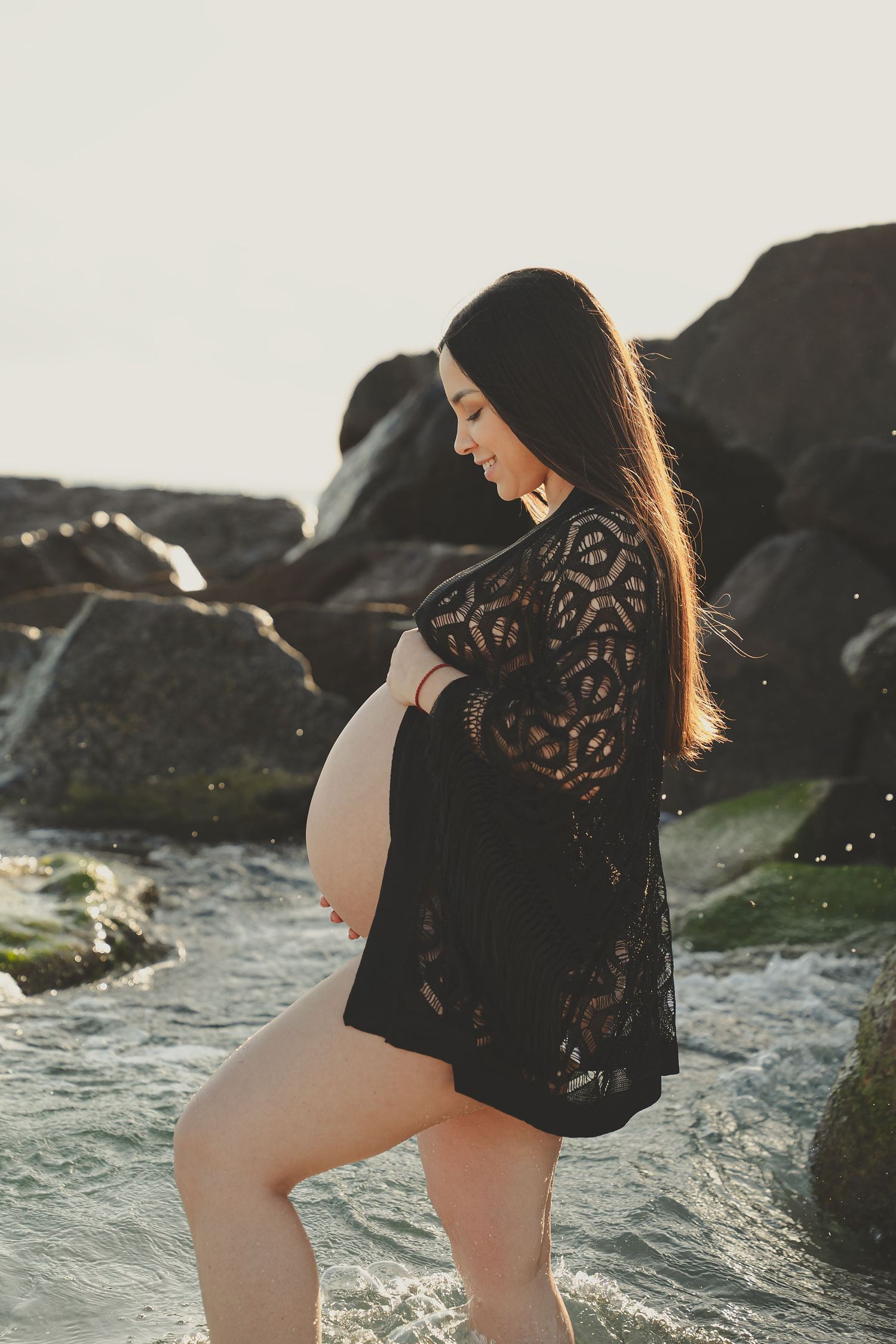 Silhouetted maternity photos against ocean waves and rocky coastline.