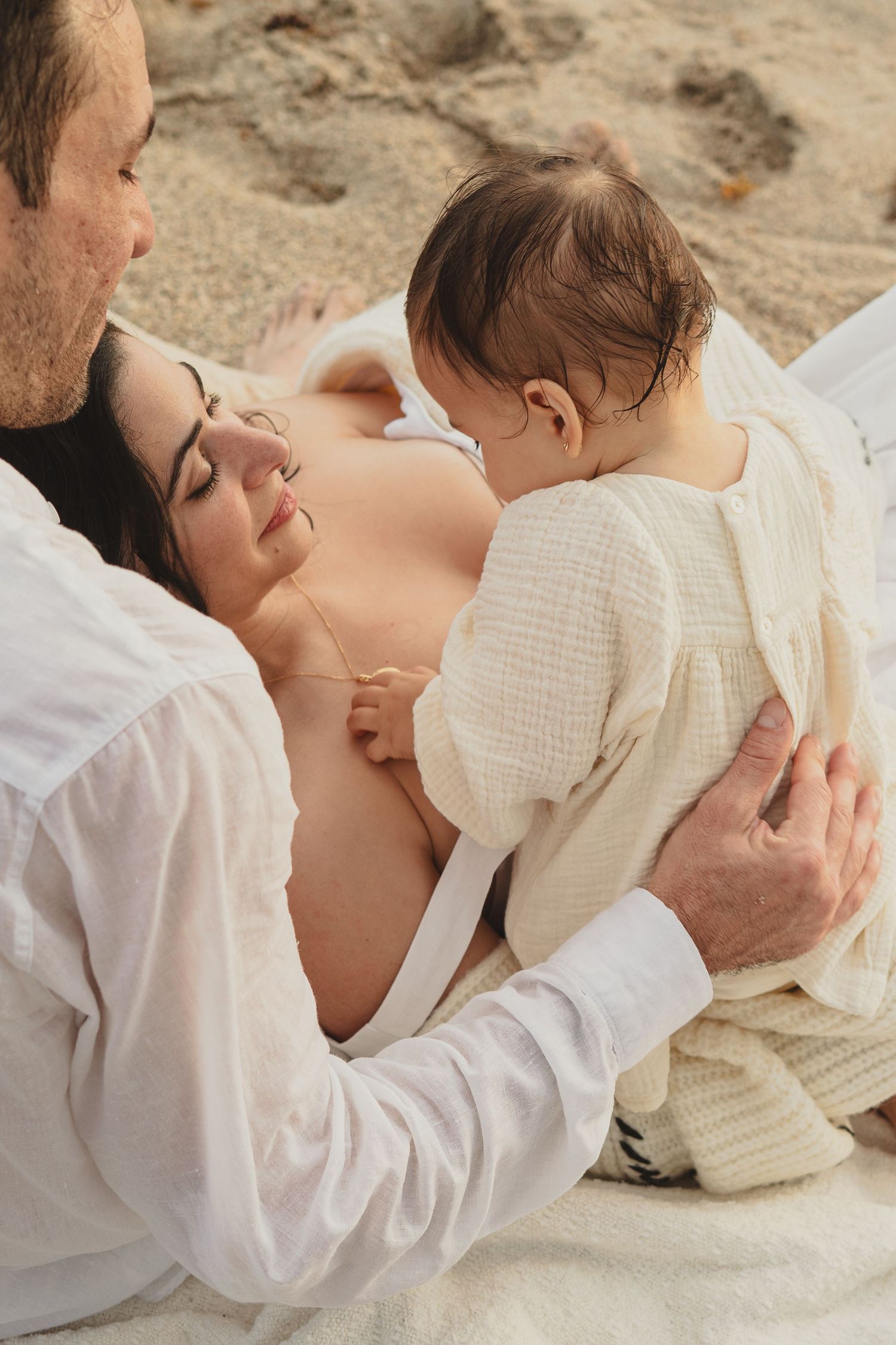 Gentle embraces between parent and child on sandy beach in cream colored clothing.