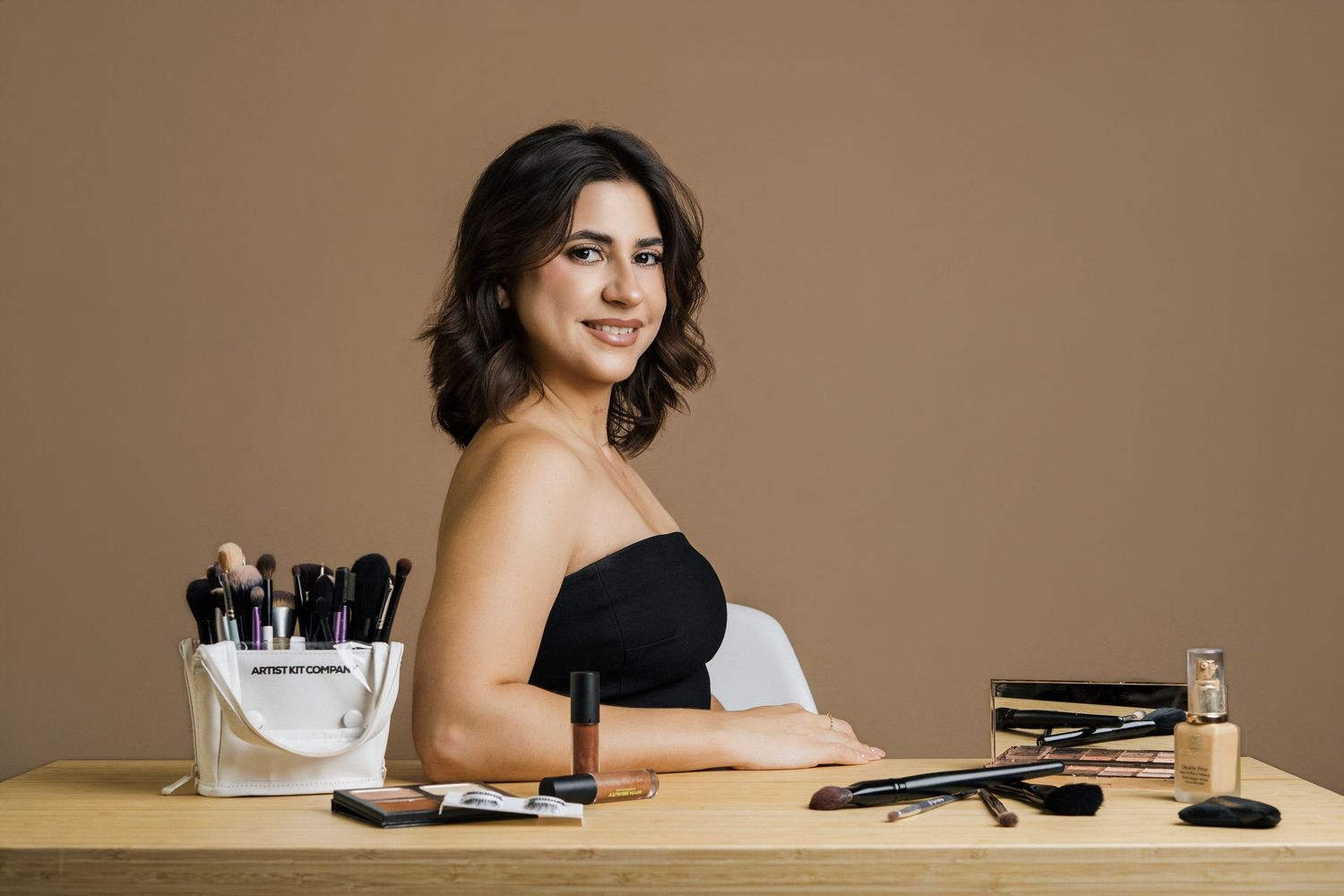 Woman in black top smiles while sitting at desk with office supplies.