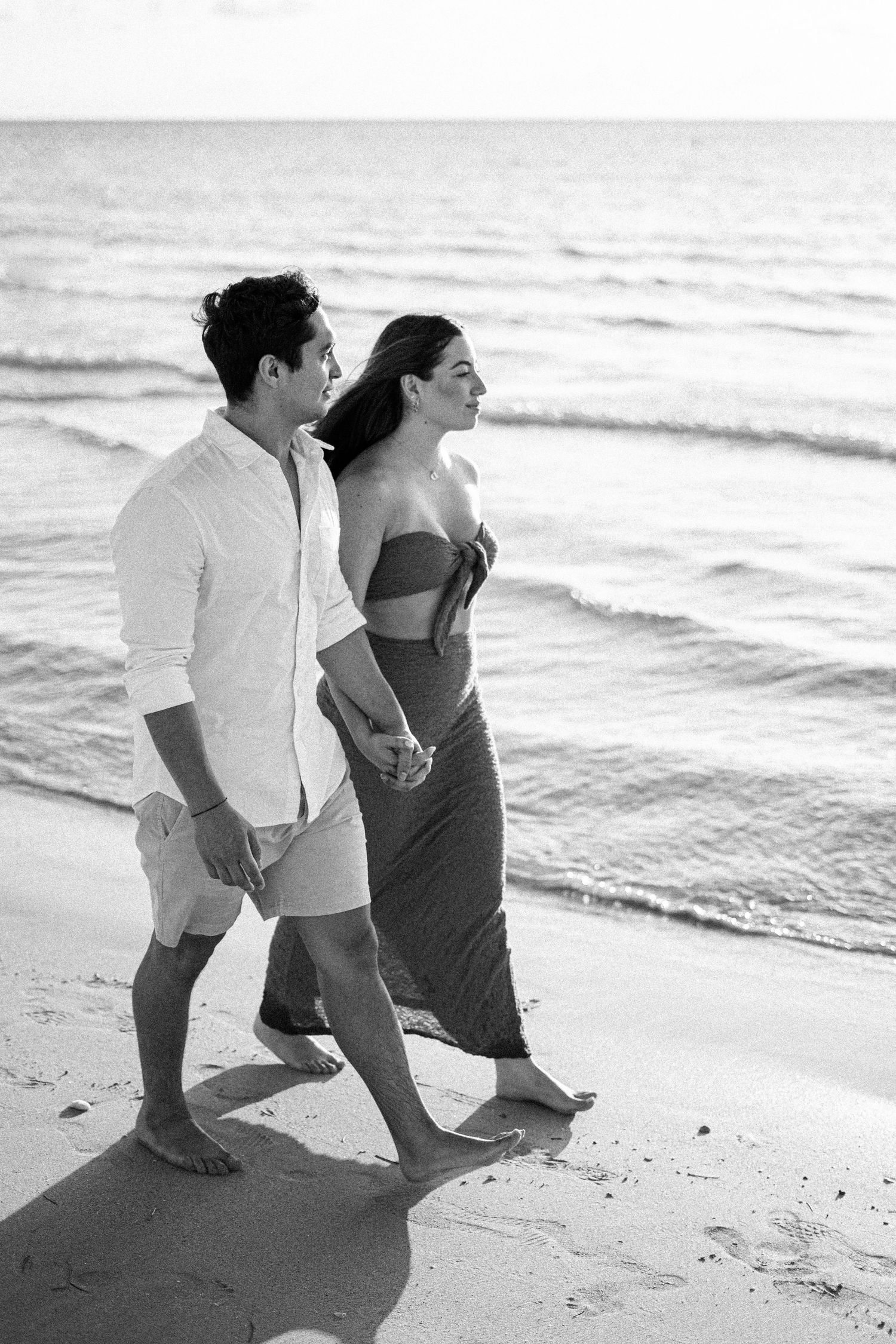 A couple takes a romantic stroll along the beach in black and white.