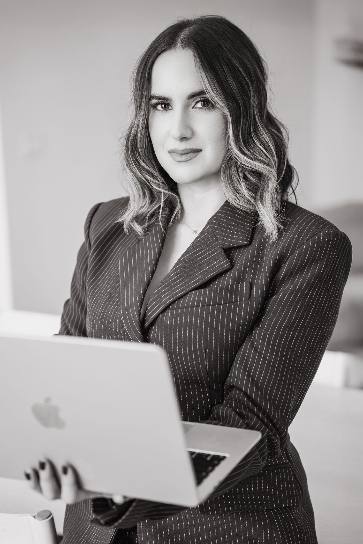 Professional woman in pinstripe suit holding MacBook laptop, black and white business portrait photography.