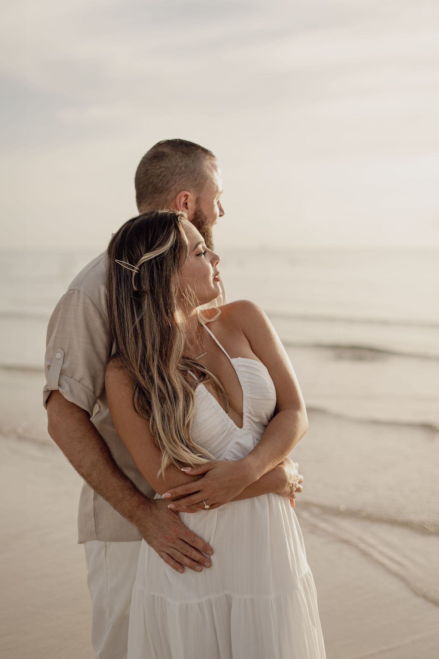 Intimate beach photography session with couple in white clothing during golden hour.