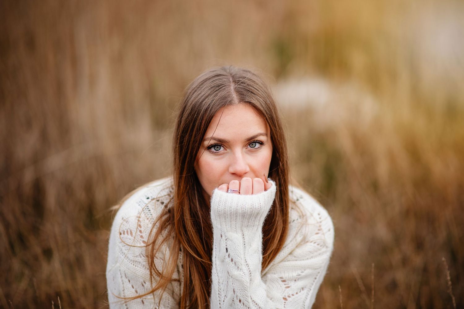 Une femme vêtue d'un pull blanc confortable est assise pensivement dans un champ de hautes herbes d'automne pendant l'heure dorée.