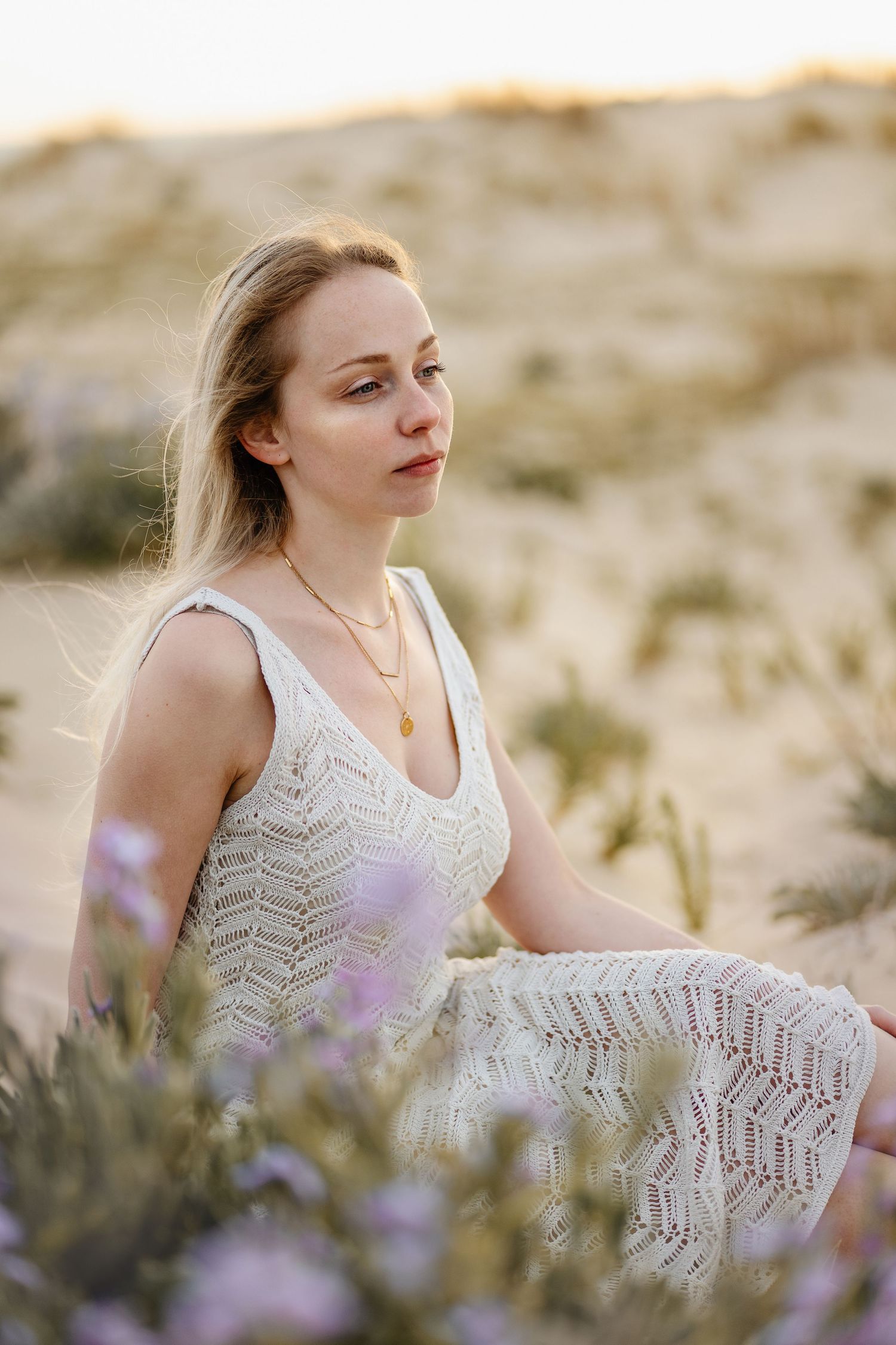 Un portrait doux dans un paysage désertique avec des fleurs sauvages présente quelqu'un portant une robe en dentelle blanche à l'heure dorée