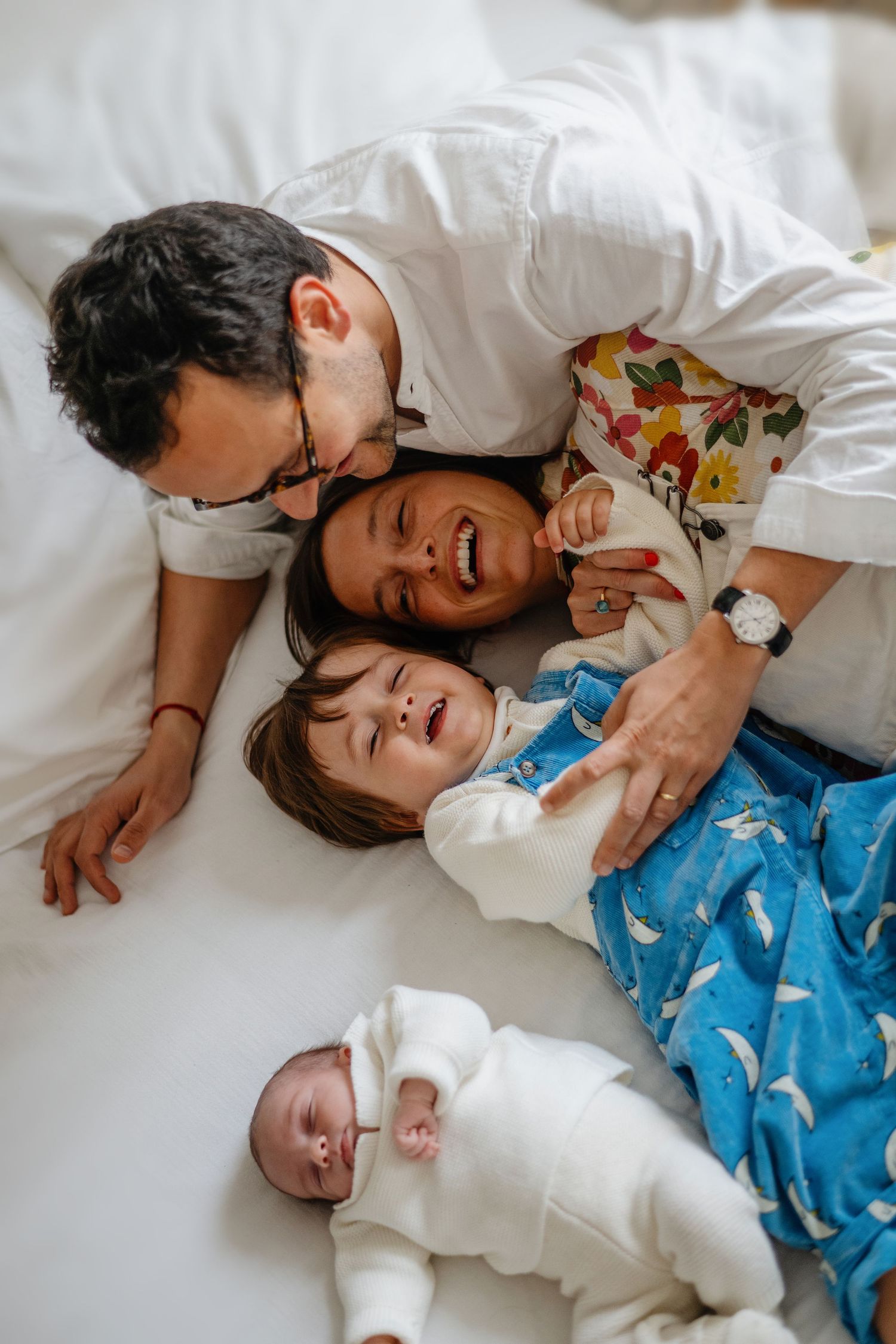 Une famille profite de moments de câlins joyeux ensemble, allongée sur une literie blanche.