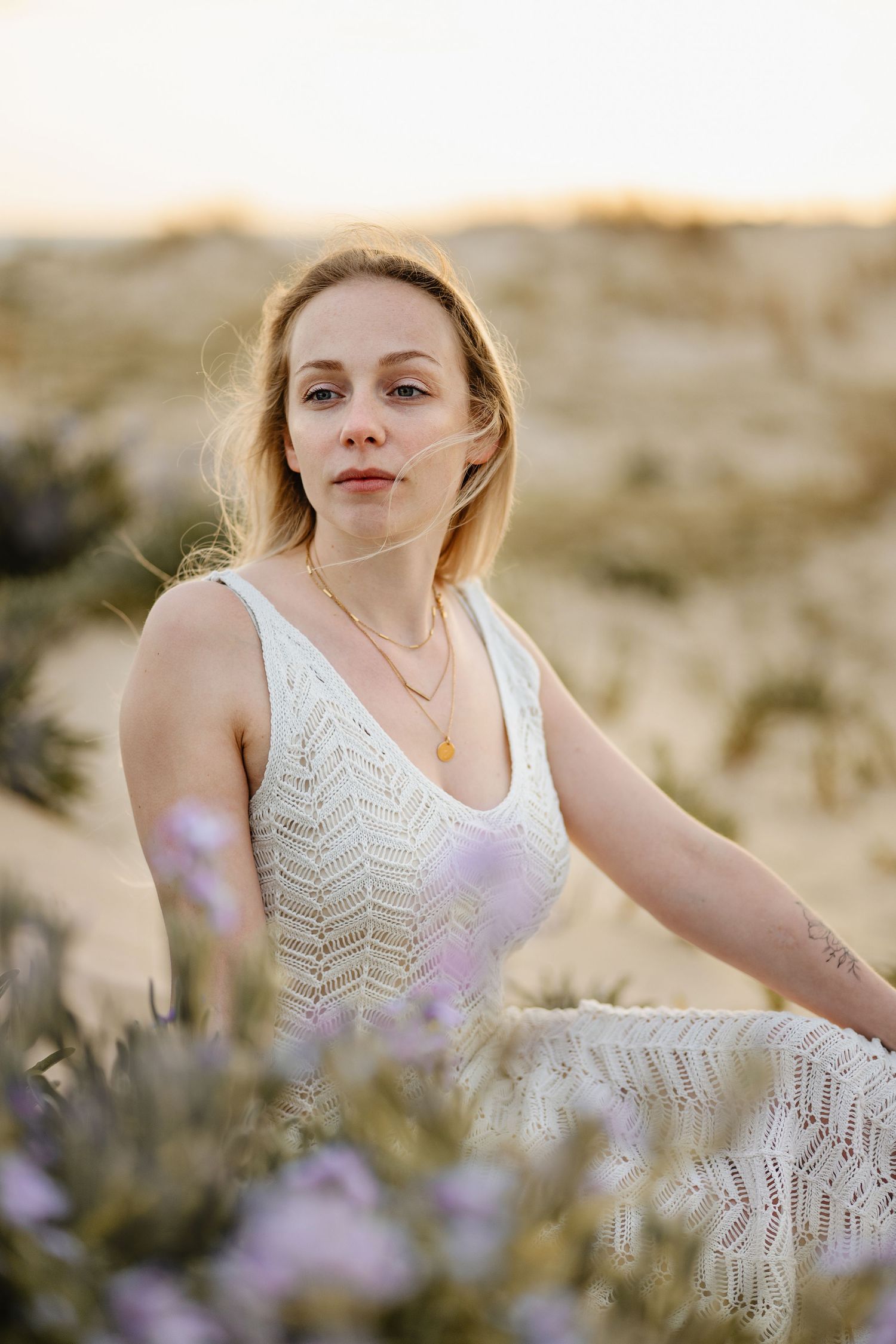 Portrait d'une personne vêtue d'une robe en dentelle blanche assise parmi des fleurs sauvages violettes au coucher du soleil dans un paysage