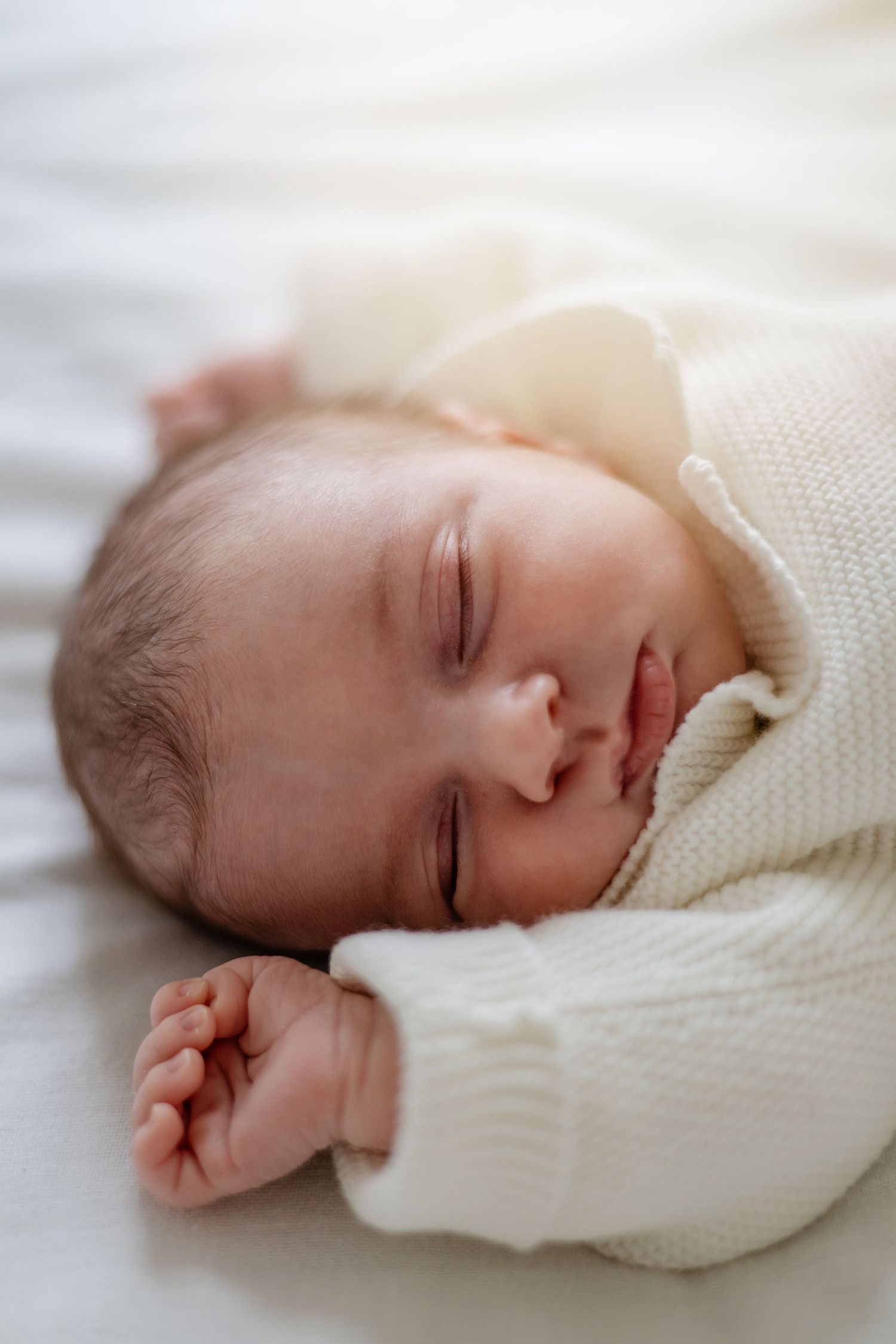 Un petit bébé dort paisiblement tout en portant un pull en tricot blanc doux sur une literie blanche.