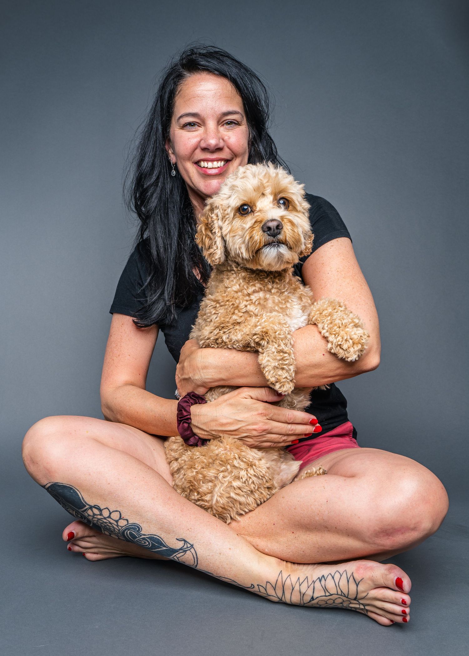 A joyful studio portrait capturing the loving bond between a woman and her fluffy companion against a simple grey backdrop.
