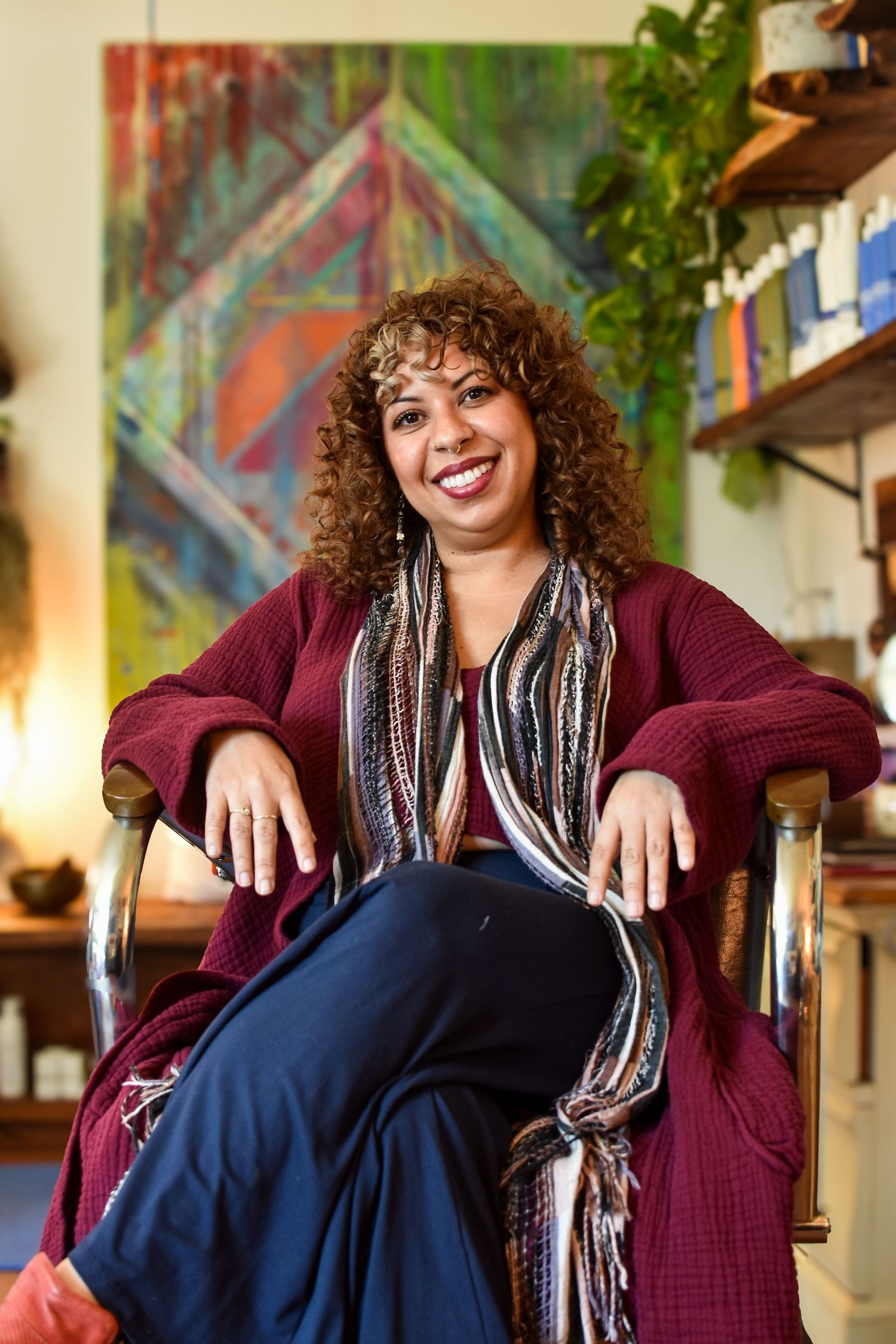 Relaxed indoor portrait wearing burgundy sweater and striped scarf in colorful artistic space.