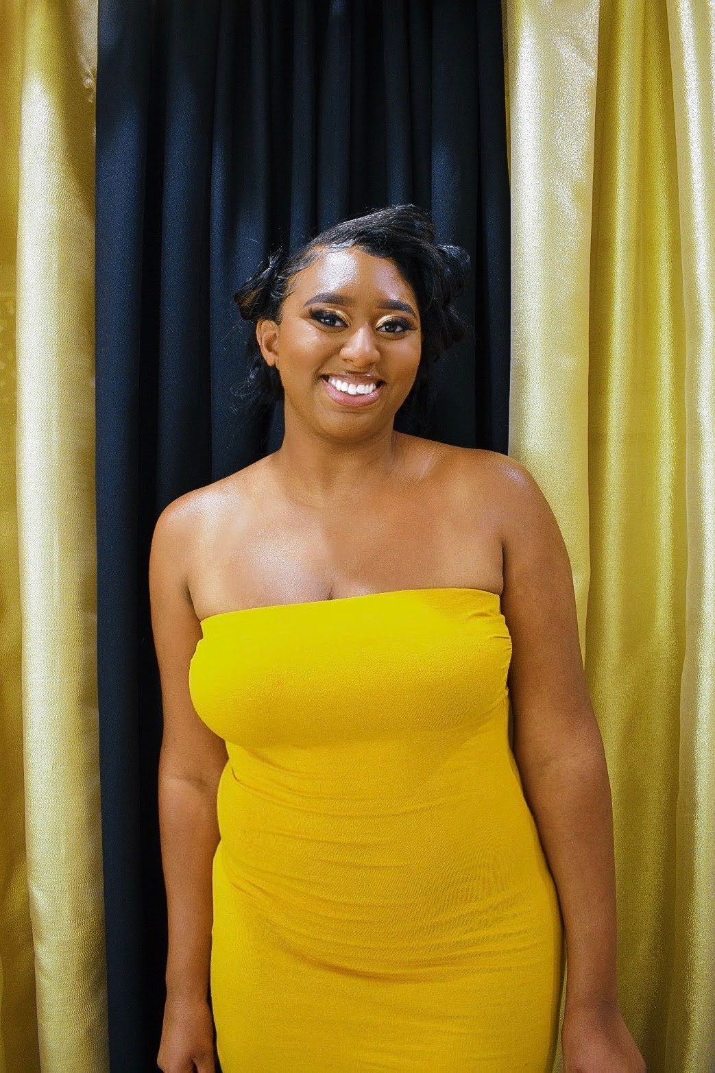 Elegant pose in bright yellow strapless dress against gold and navy curtains.