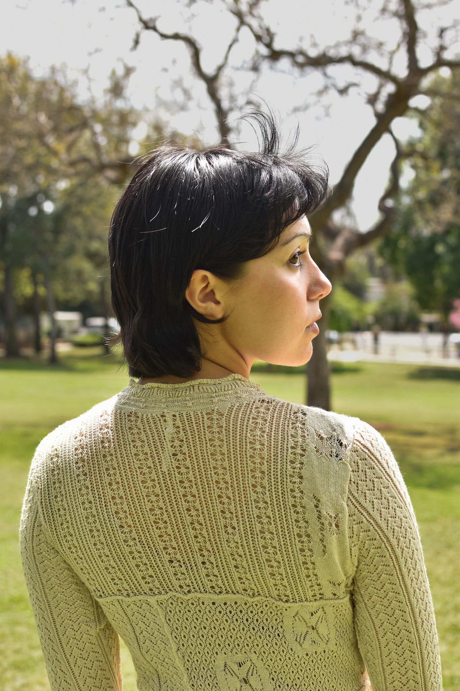 Back view of a detailed cream knitted sweater with intricate cable patterns in an outdoor garden setting.