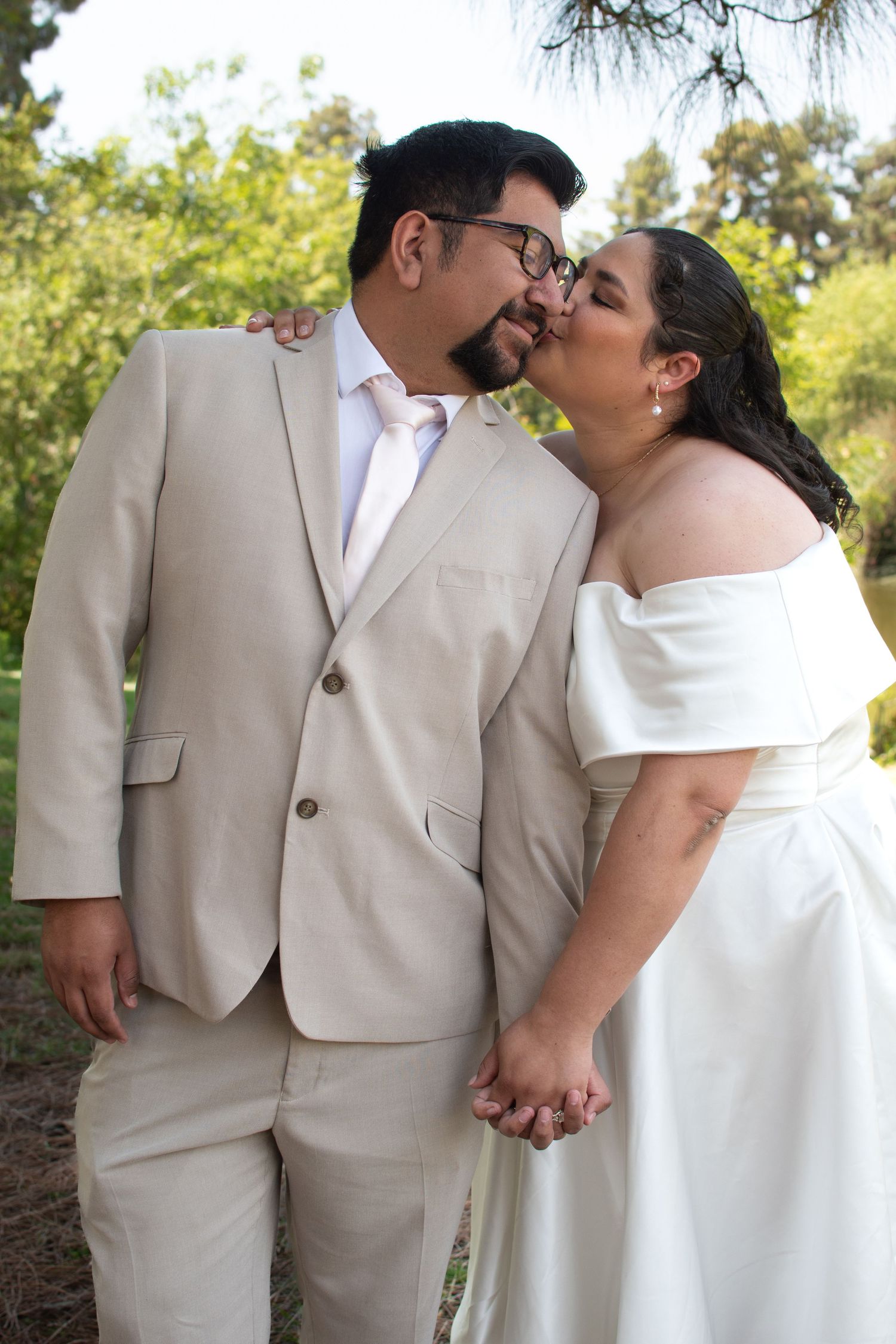 A romantic wedding couple shares tender moments in a garden setting wearing beige and white attire.
