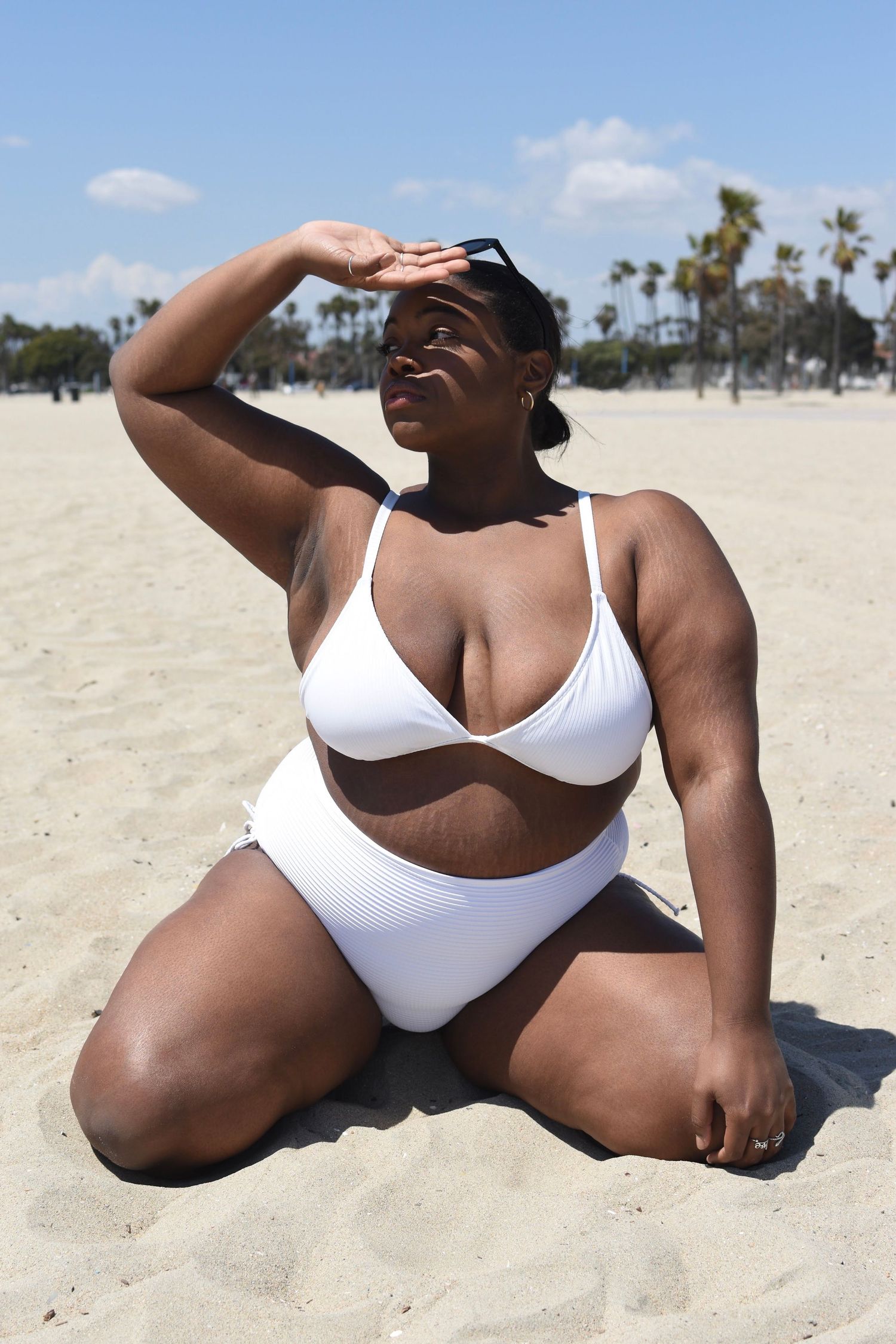 White two-piece swimsuit photographed on sandy beach with palm trees.