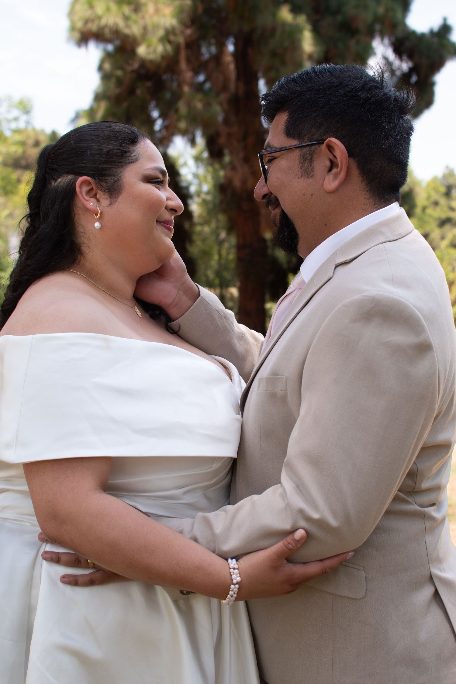 A happy couple shares an intimate moment outdoors in coordinating beige and white wedding attire.