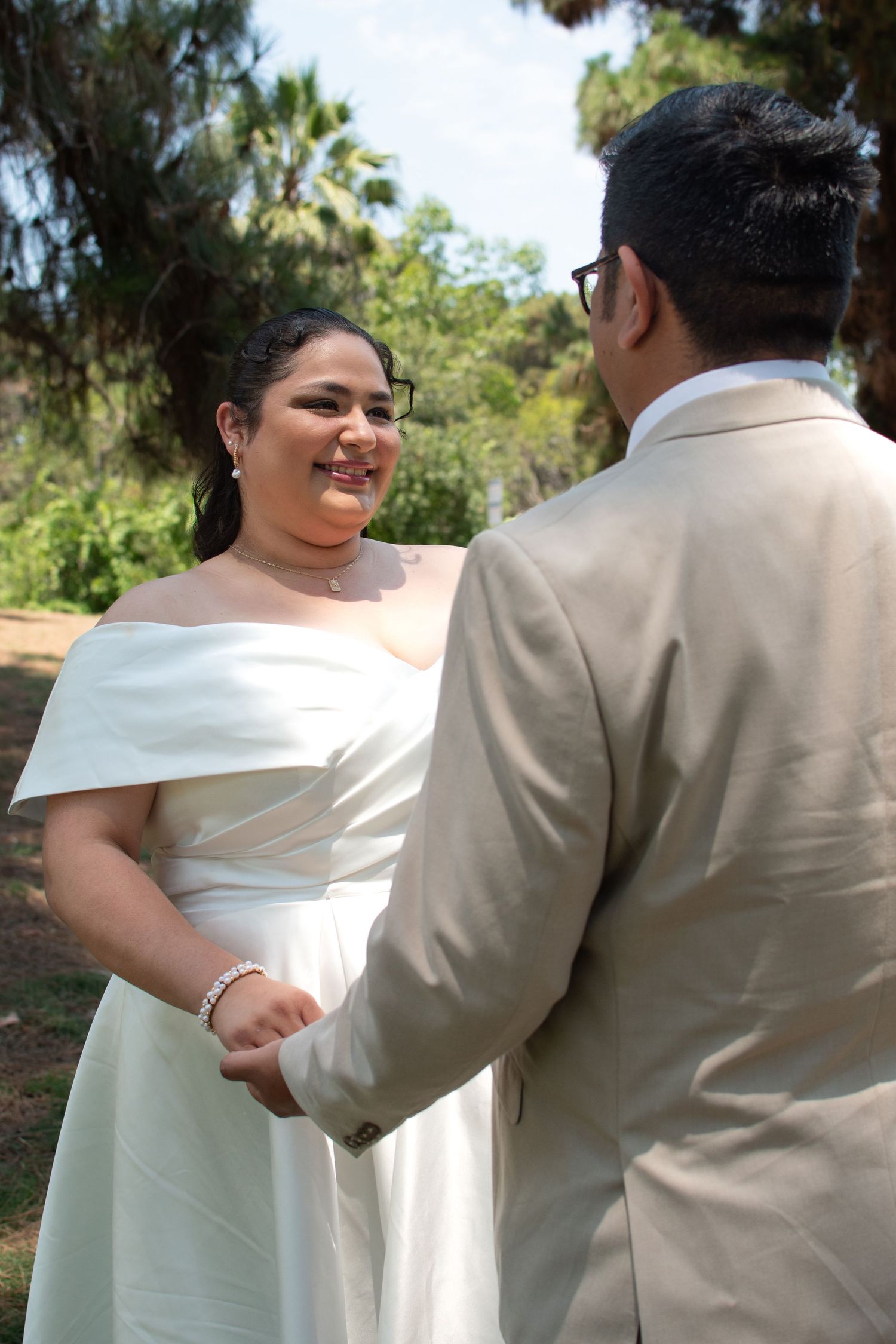 A bride and groom share a joyful moment outdoors with palm trees and greenery in the background on their wedding day.
