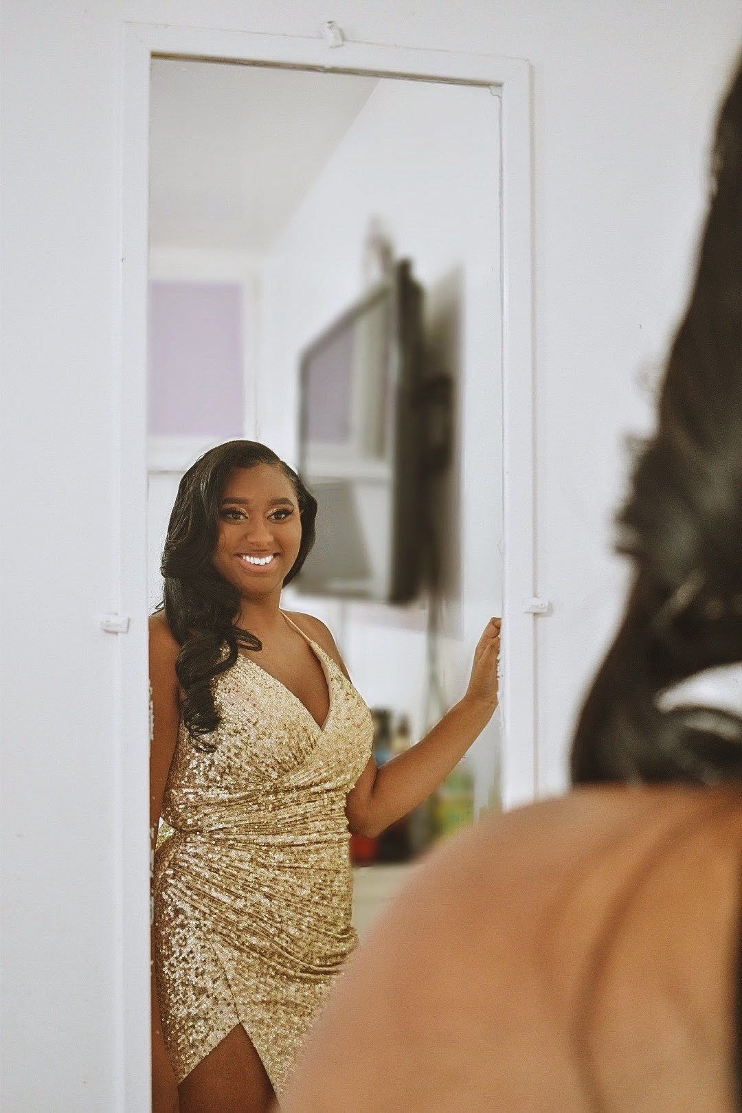 Mirror reflection captures elegant pose in shimmering gold evening gown.