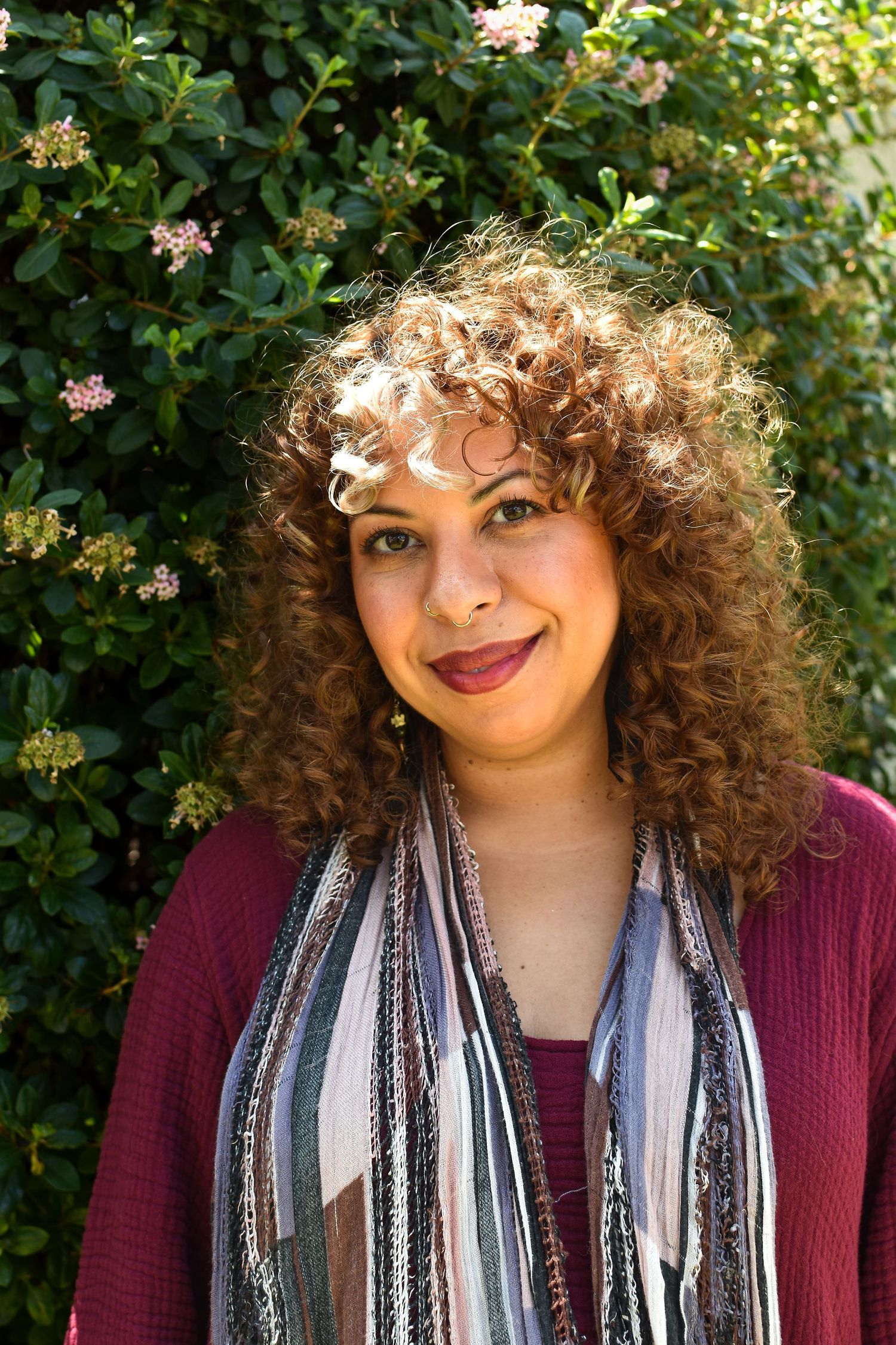 Candid portrait series showing different expressions against a leafy garden backdrop with burgundy top.