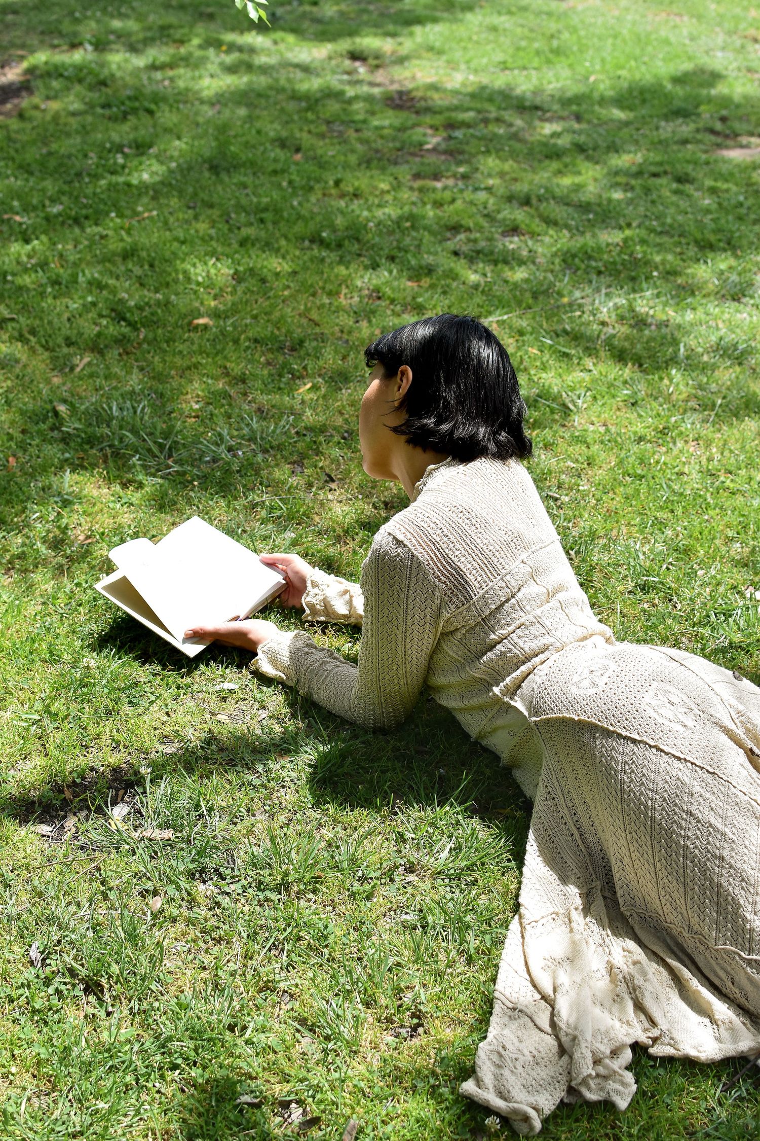 Reading in the park while wearing a vintage-style cream knit dress.