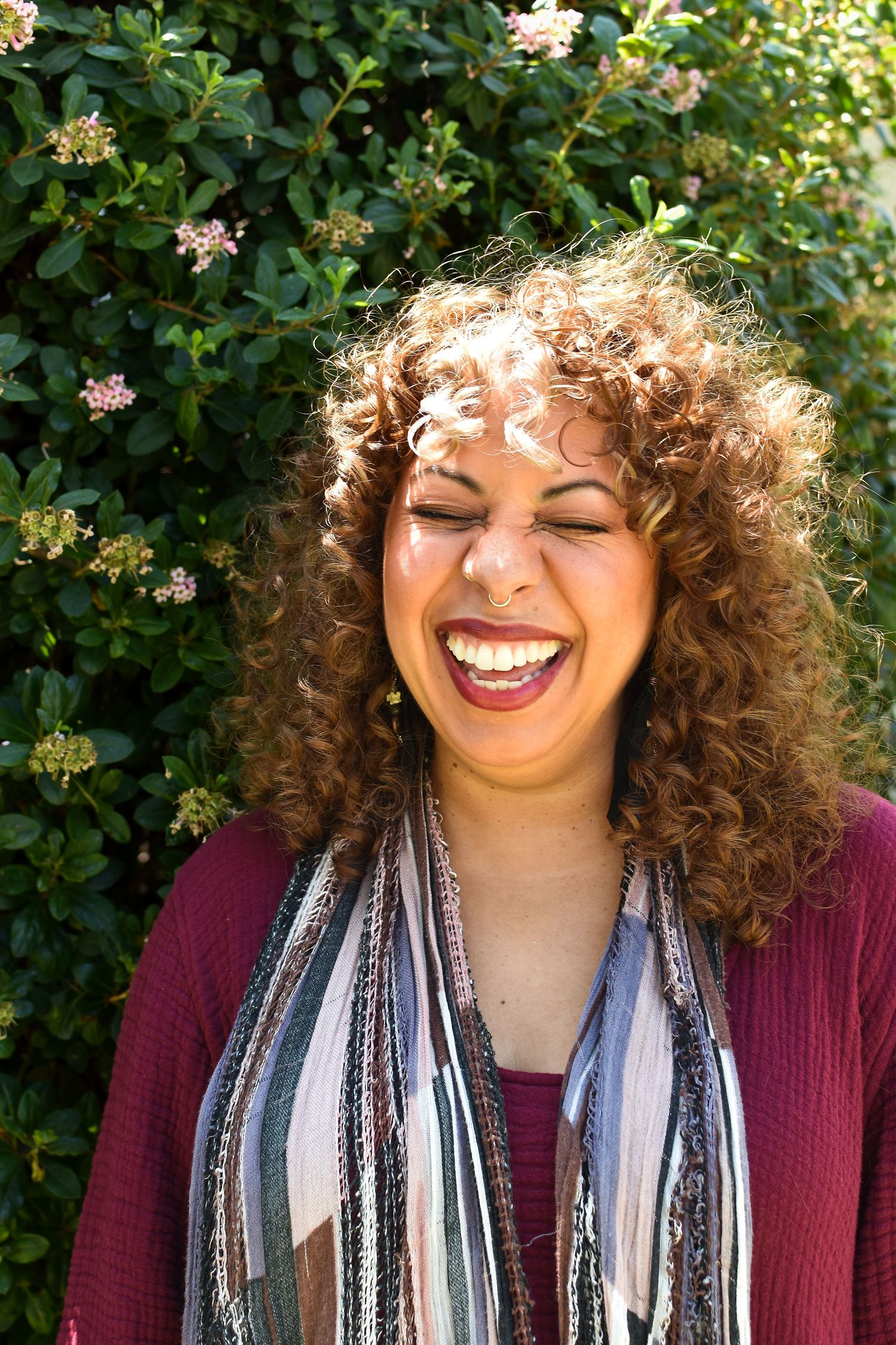 Close-up outdoor photo of someone wearing a striped scarf and burgundy sweater with flowers in background.